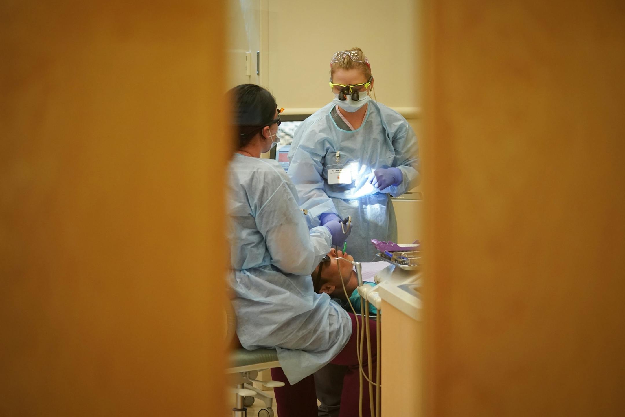 Second year dental students Elizabeth Wilder (left) and Katherine Rolek were seen through a door as they worked on a patient inside Community Dental Care in Maplewood. The two students were part of a group of 35 who continued their education and training through Century College after the abrupt closing of Argosy Univeristy.