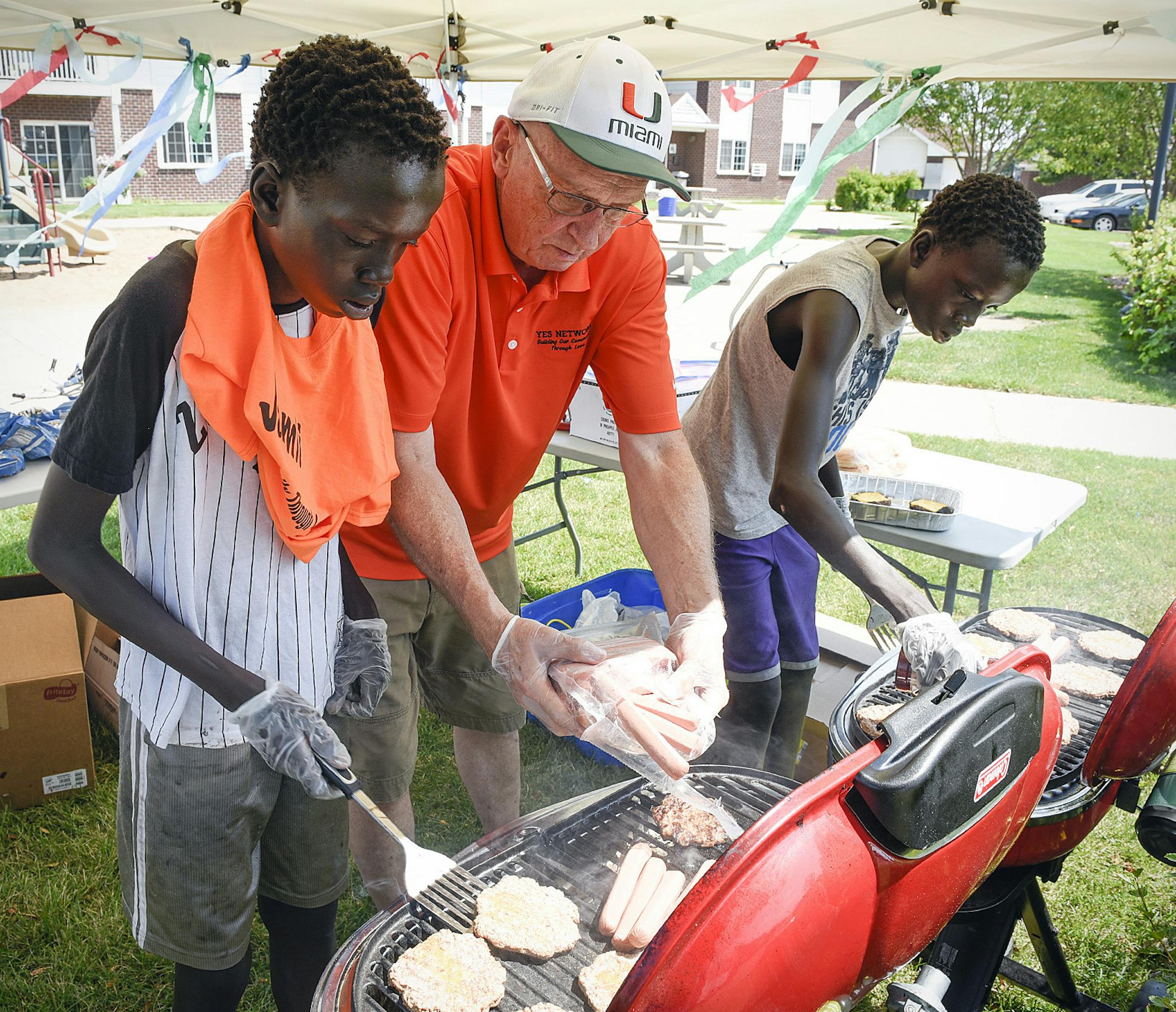 FOR RELEASE MONDAY, AUGUST 8, 2016, AT 12:01 A.M. CDT.-Jerry Sparby of the YES Network, center, put hot dogs and hamburgers on the grill for Jack Hoth, 14, left, and his twin brother Chang, right, as the made lunch Wednesday, July 20, 2016, at the Westwood Village Apartments in St. Cloud, Minn. (St. Cloud Times/Jason Wachter via AP)