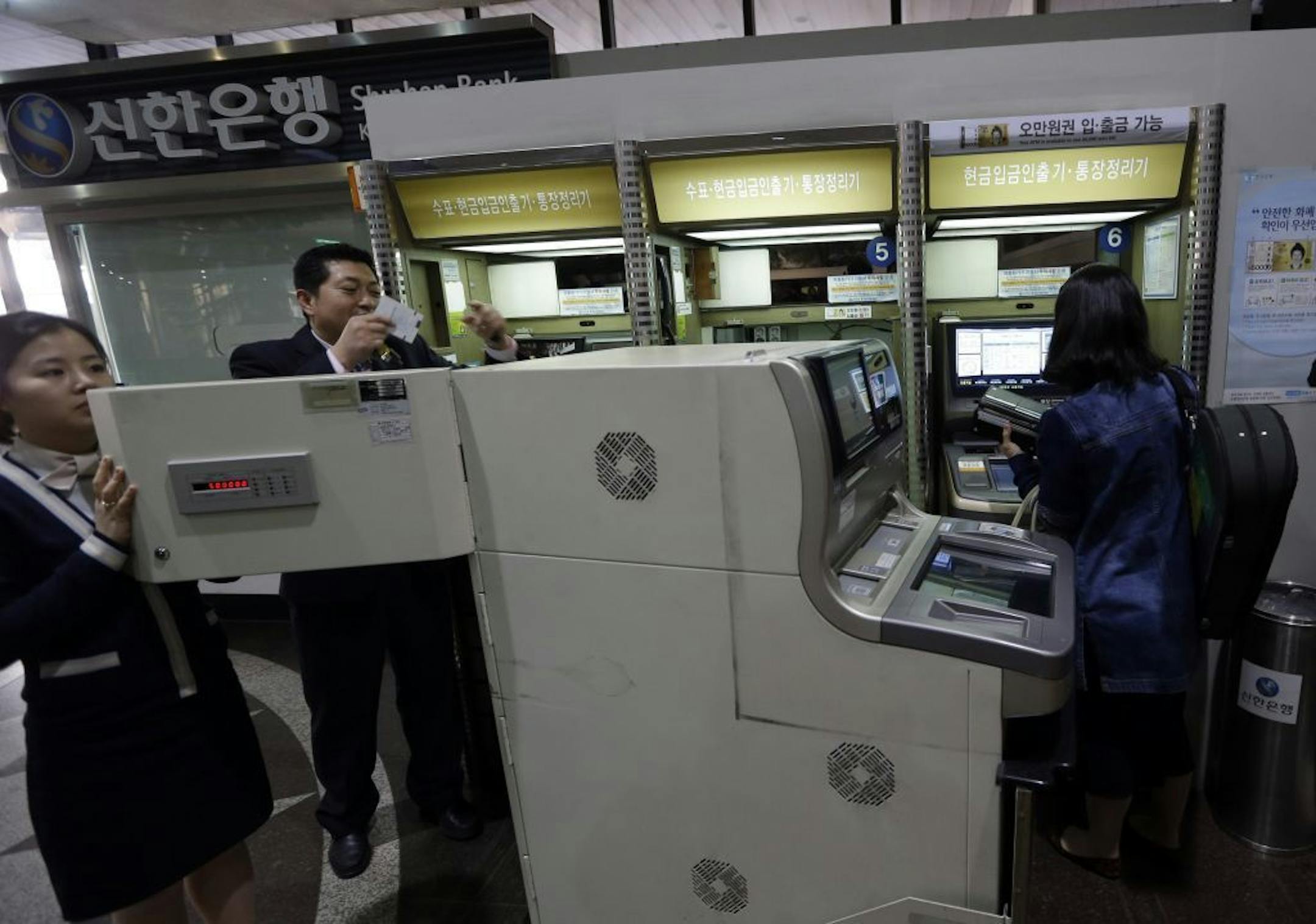 Two bank clerks, left, check an automated teller machine at a branch of Shinhan Bank after the bank's computer networks are fixed in Seoul, South Korea, Wednesday, March 20, 2013. Computers networks at two major South Korean banks and three top TV broadcasters went into shutdown mode en masse Wednesday, paralyzing bank machines across the country and prompting speculation of a cyberattack by North Korea.