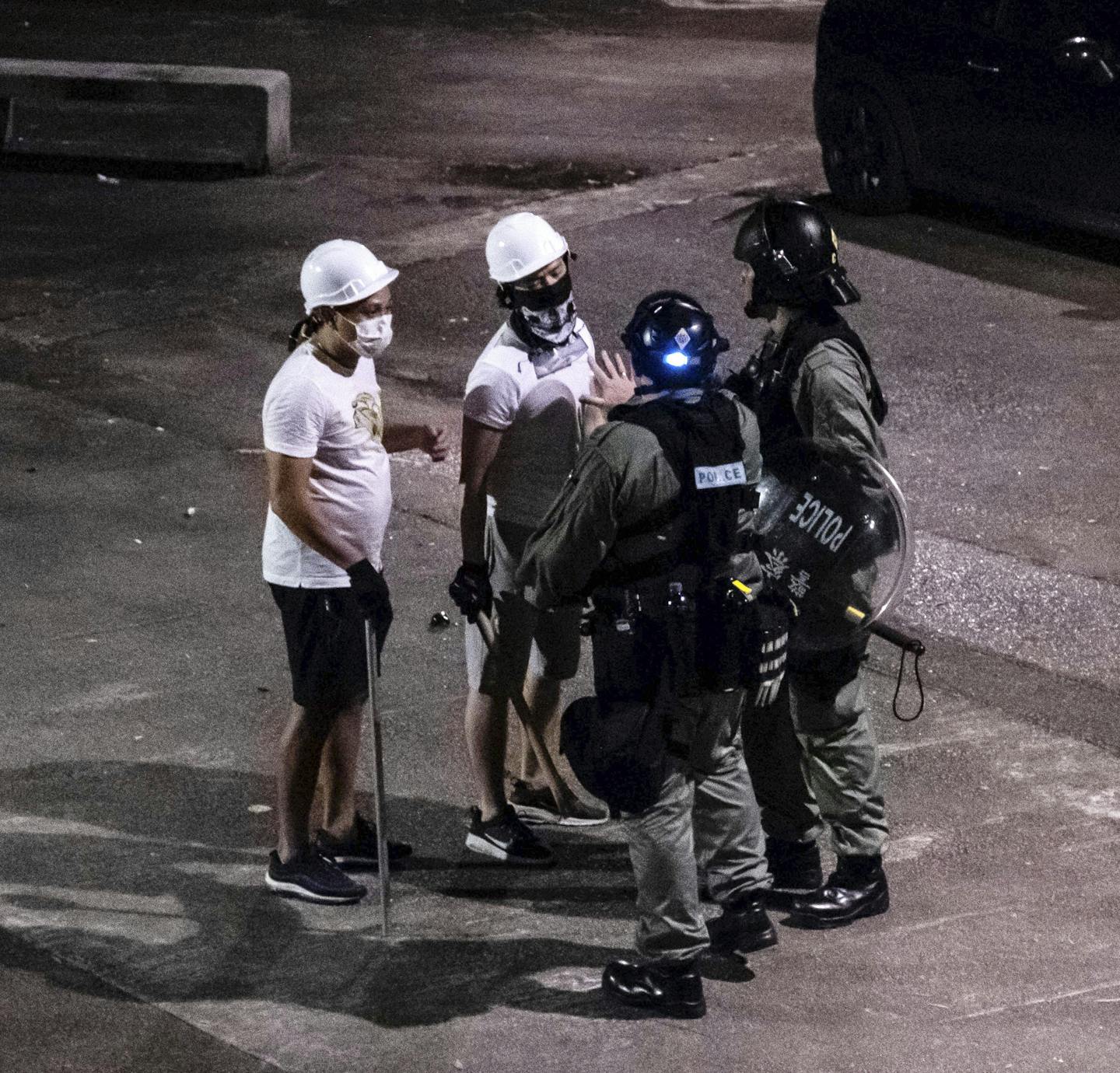 FILE -- Hong Kong police officers speak to men armed with poles after a mob attacked people at a train station in the Yuen Long district of Hong Kong, July 21, 2019. The police in Hong Kong arrested a prizewinning journalist on Tuesday whose work had exposed the authorities' delayed response to a mob attack on antigovernment protesters last year. (Lam Yik Fei/The New York Times)