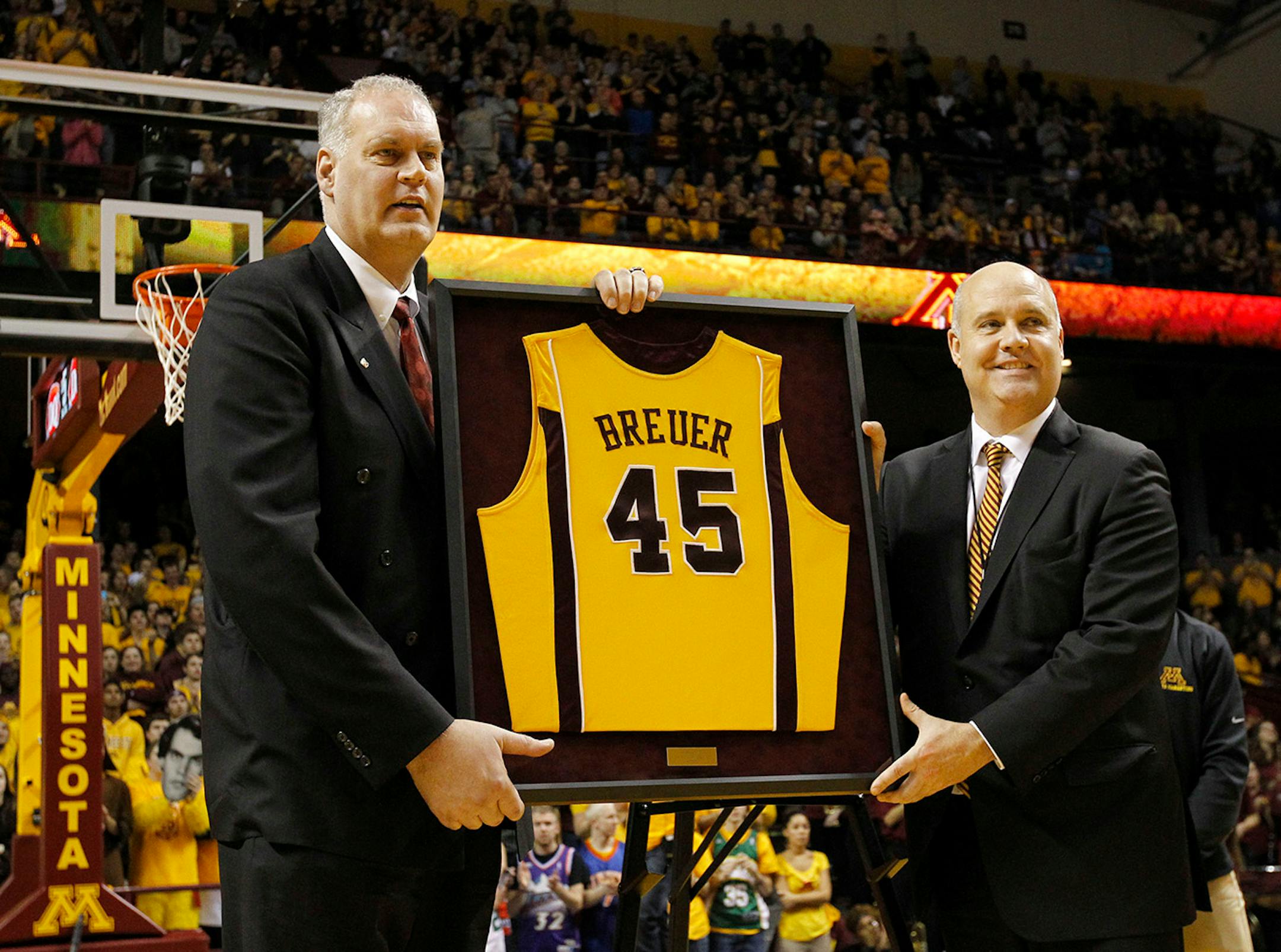 Former Minnesota and NBA player Randy Breuer, left, joins Minnesota Athletic Director Norwood Teague, right, during a ceremony to retire Breuer's jersey at half-time of an NCAA college basketball game against Illinois in Minneapolis, Saturday, Jan. 24, 2015. (AP Photo/Ann Heisenfelt)
