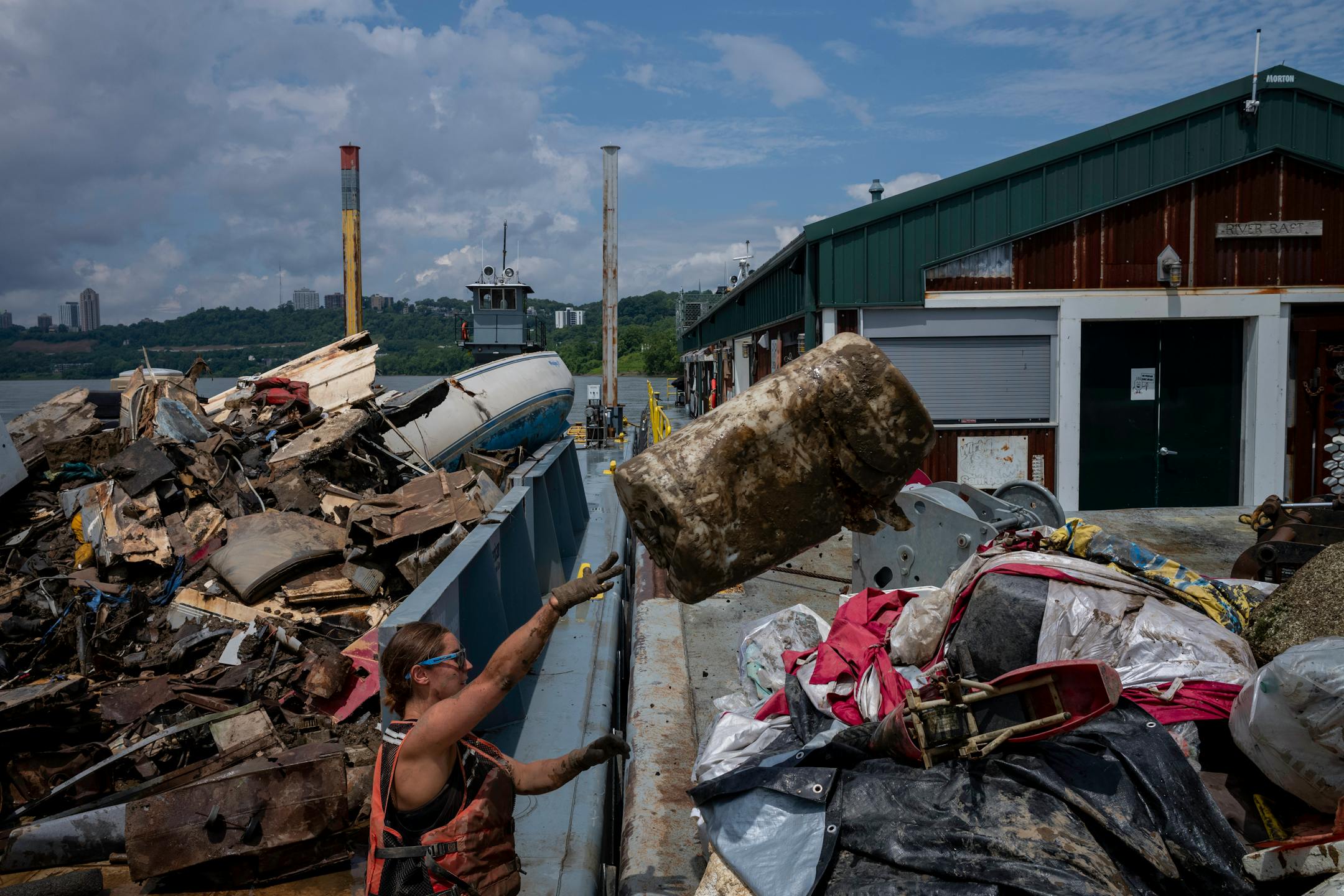Rachel Loomis tosses a plastic barrel onto the barge on Tuesday, July 13, 2021 in Cincinnati, Ohio. As trash is gathered, it's brought back to their barge, where they sort and store it before taking it and disposing of it properly.