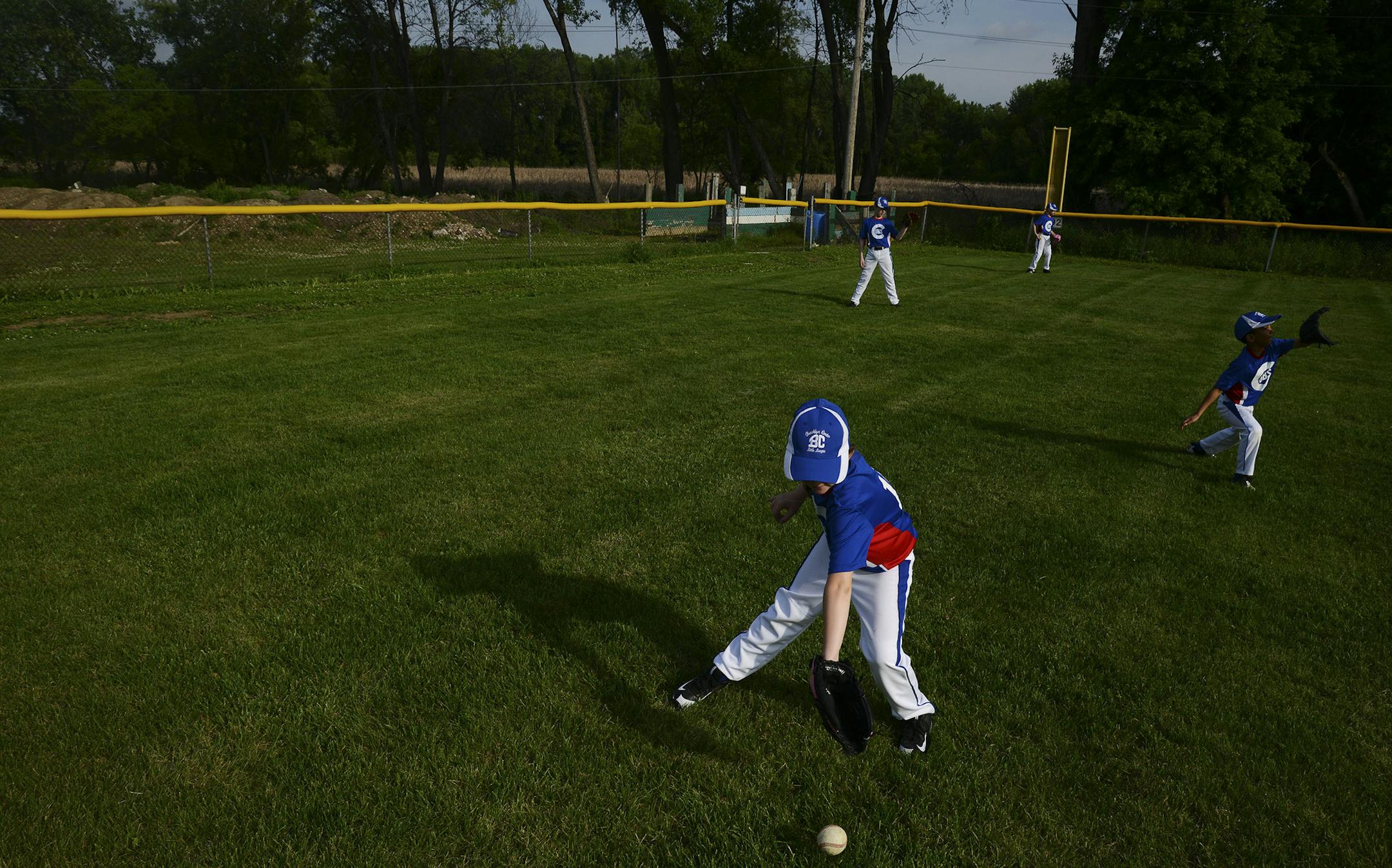 Front, Genevieve Rose, 8, of Brooklyn Center, reached down to grab the ball during the Little League Cub's warm-up in Brooklyn Center, Minn., on Thursday June 4, 2015. Behind Rose and her teammates, mounds of dirt and concrete sat next to the little league baseball diamond. The site has become an illegal dumpsite containing concrete and mounds of dirt. ] RACHEL WOOLF rachel.woolf@startribune.com