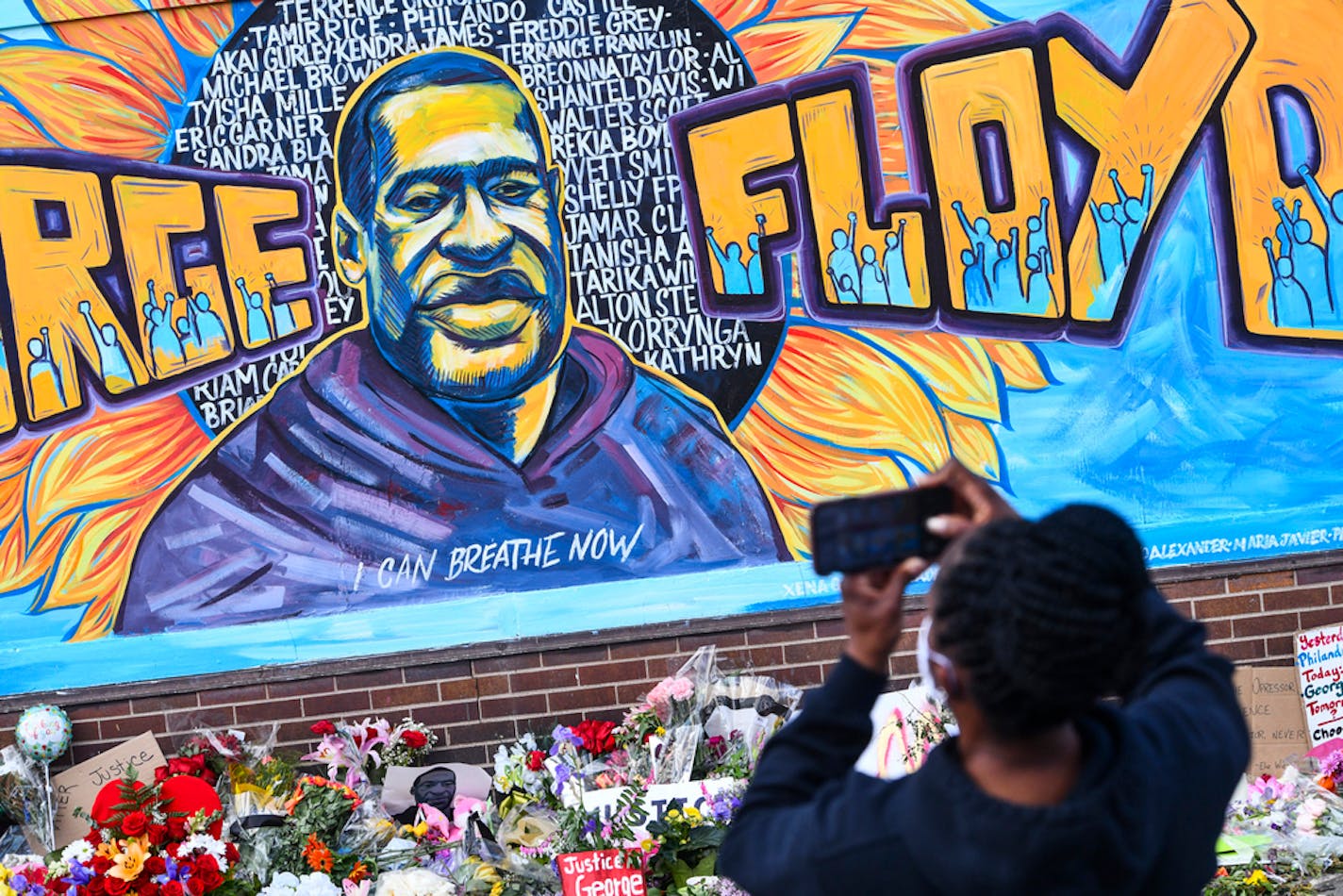 A person takes photographs of a mural in memory of George Floyd with flowers and other memorial items below, on a wall of the Cup Foods store at the corner of Chicago Avenue and East 38th Street, Friday, May 29, 2020, in Minneapolis. Protests over the death of Floyd in Minneapolis police custody have spread to other areas across the United States. (Dave Schwarz/St. Cloud Times via AP)