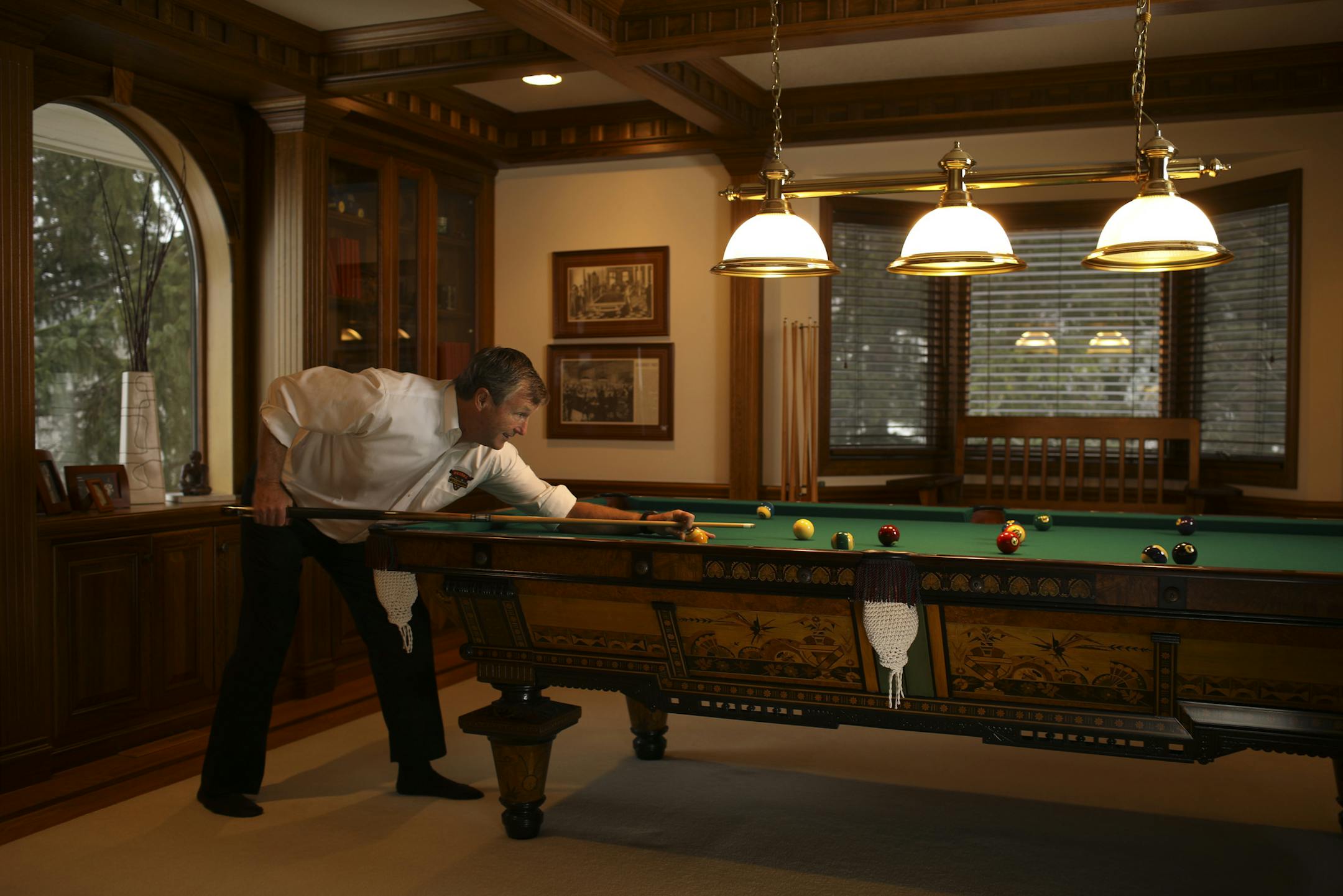 Greg Peterson lines up a shot at a restored antique pool table, one of four in his Edina home.