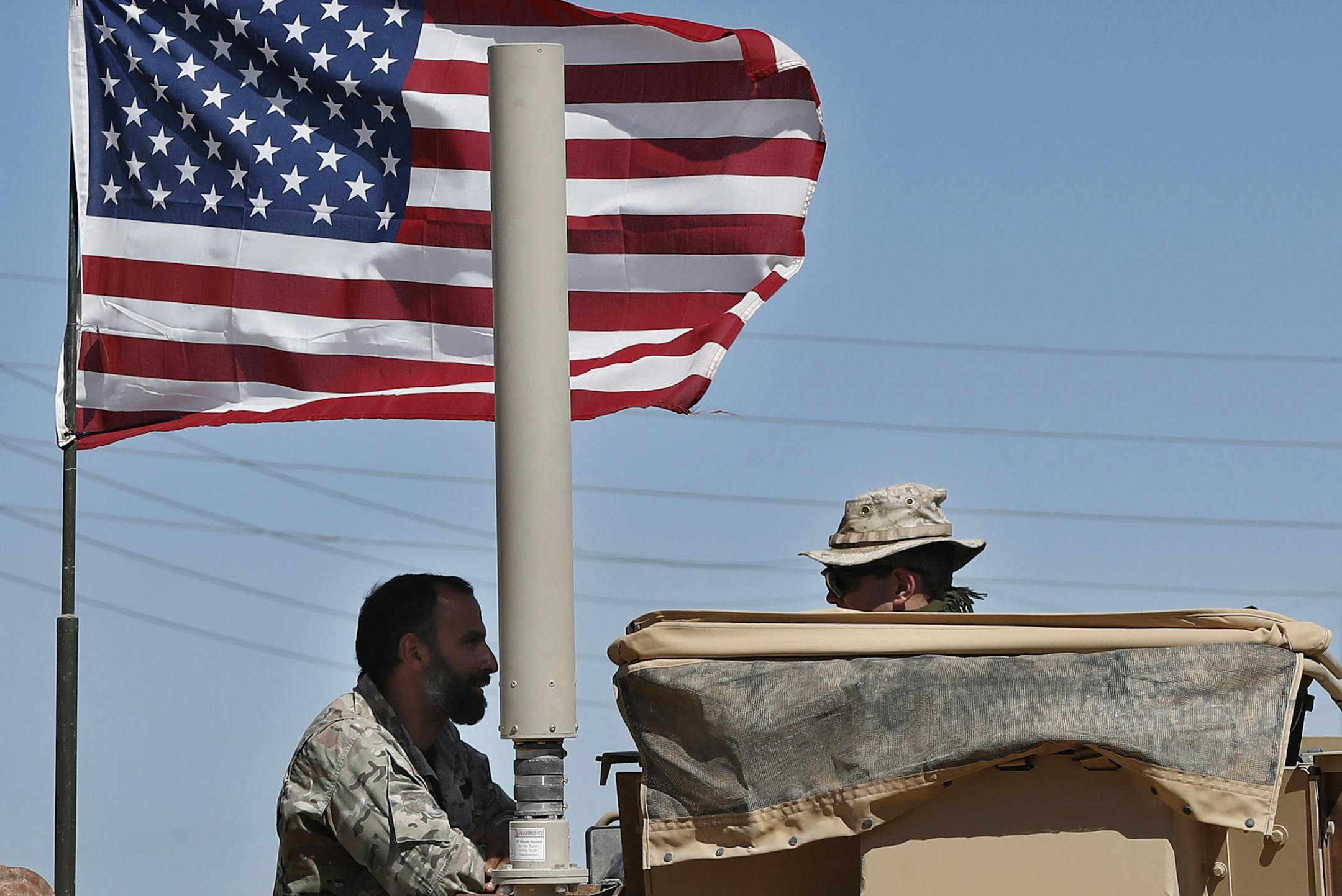 In this April 4, 2018 photo, a U.S-backed Syrian Manbij Military Council soldier, left, speaks with a U.S. soldier, at a U.S. position near the tense front line with Turkish-backed fighters, in Manbij town, north Syria. President Donald Trump's decision to withdraw troops from Syria has rattled Washington's Kurdish allies, who are its most reliable partner in Syria and among the most effective ground forces battling the Islamic State group. Kurds in northern Syria said commanders and fighters me