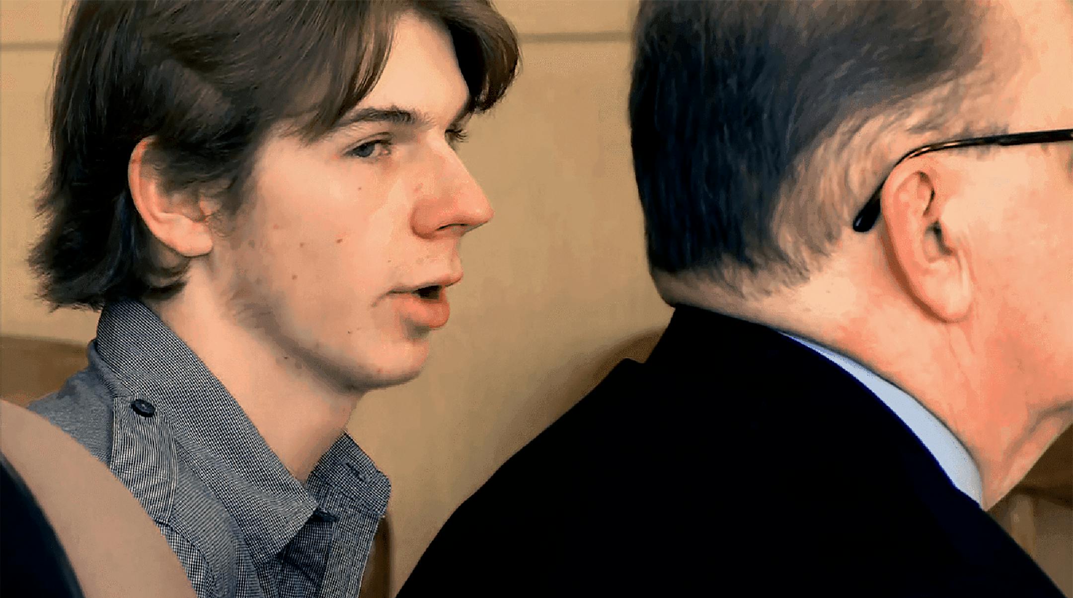 Closeup of defendant in court wearing black and white checked shirt with male attorney in black suit.