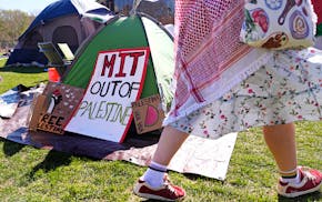 A woman walks past a sign where students protest at an encampment on the campus of the Massachusetts Institute of Technology, Tuesday, April 23, 2024,