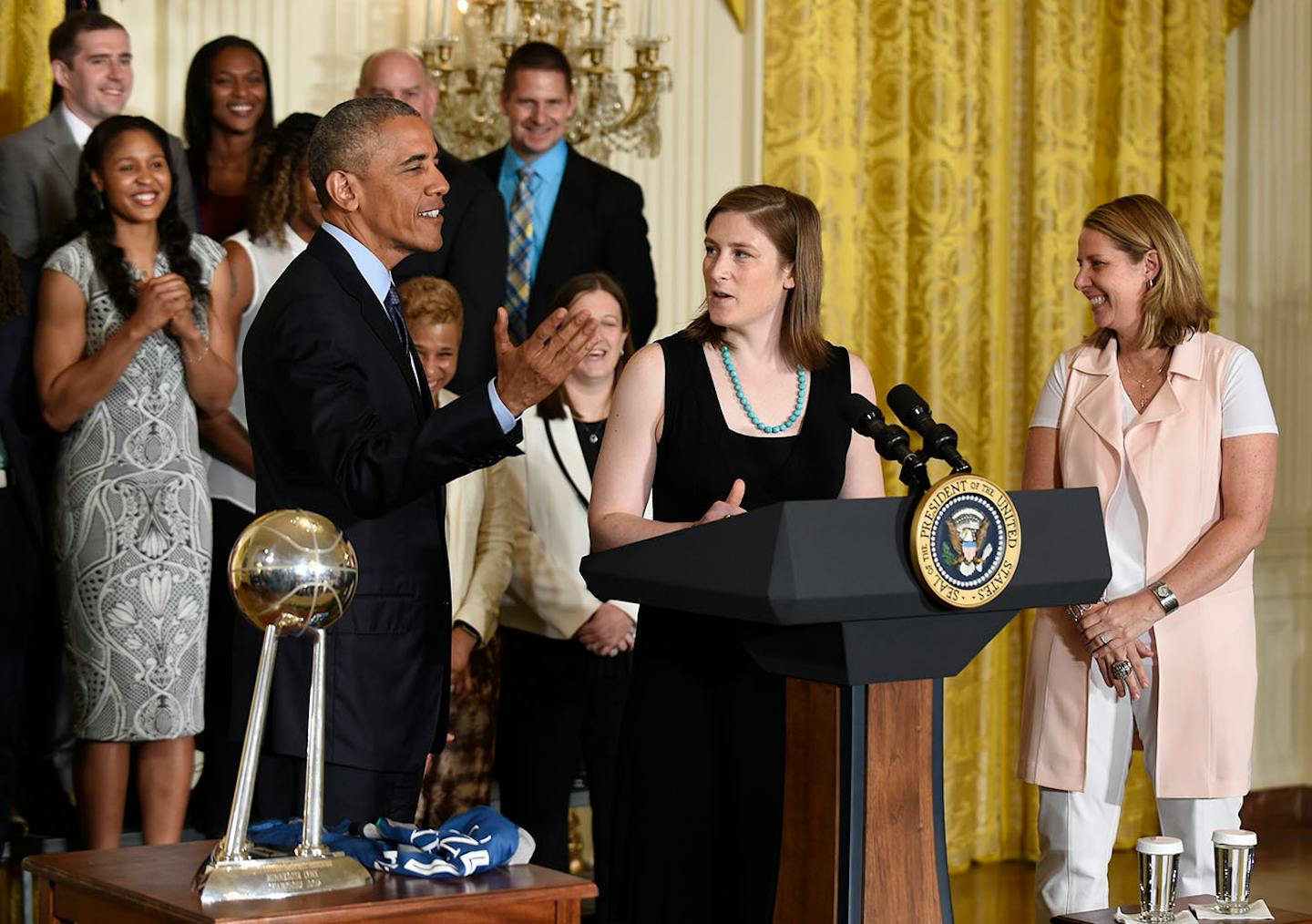 President Barack Obama, front left, listens as Minnesota Lynx player Lindsay Whalen, center, speaks in the East Room of the White House in Washington, Monday, June 27, 2016, during a ceremony where Obama honored the 2015 WNBA basketball Champion Minnesota Lynx. Coach Cheryl Reeve listens at right.