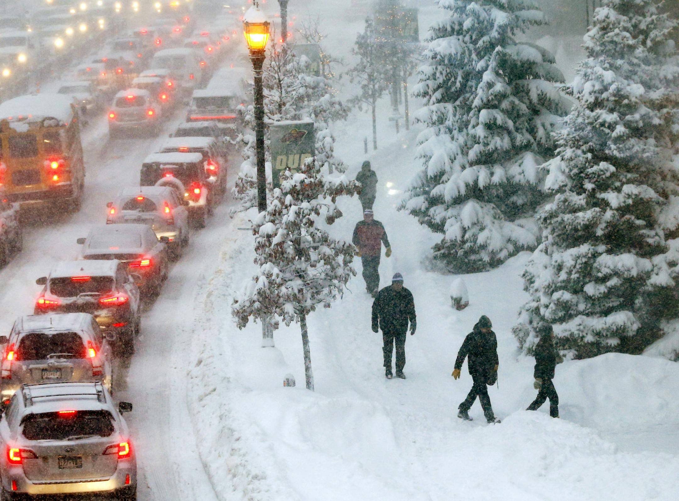 Backup traffic waits at a light as pedestrians arrive at Xcel Arena for a Minnesota Wild and Ottawa Senators NHL hockey game Monday, Jan. 22, 2018, in St. Paul, Minn. as heavy snow and strong winds are pushing through the Midwest. (AP Photo/Jim Mone)