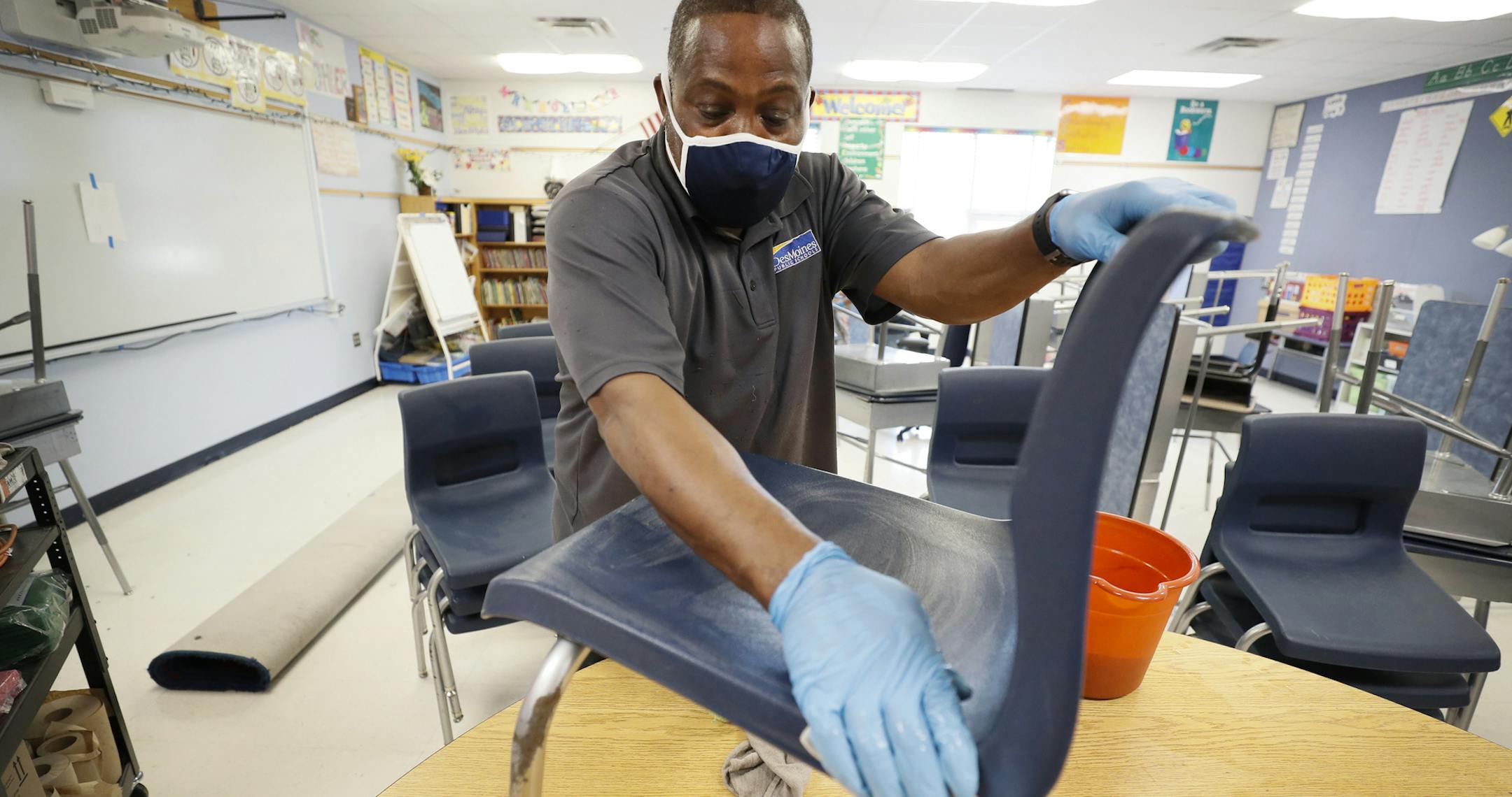 Des Moines Public Schools custodian Tracy Harris cleans a chair in a classroom at Brubaker Elementary School, Wednesday, July 8, 2020, in Des Moines, Iowa. School districts that plan to reopen classrooms in the fall are wrestling with whether to require teachers and students to wear face masks. In Iowa, among other places, where Democratic-leaning cities like Des Moines and Iowa City have required masks to curb the spread of the coronavirus, while smaller, more conservative communities have left