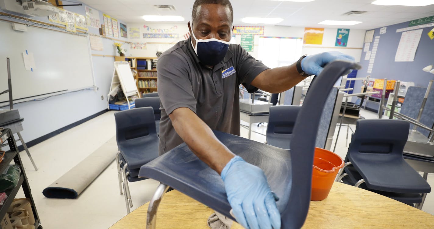 Des Moines Public Schools custodian Tracy Harris cleans a chair in a classroom at Brubaker Elementary School, Wednesday, July 8, 2020, in Des Moines, Iowa. School districts that plan to reopen classrooms in the fall are wrestling with whether to require teachers and students to wear face masks. In Iowa, among other places, where Democratic-leaning cities like Des Moines and Iowa City have required masks to curb the spread of the coronavirus, while smaller, more conservative communities have left