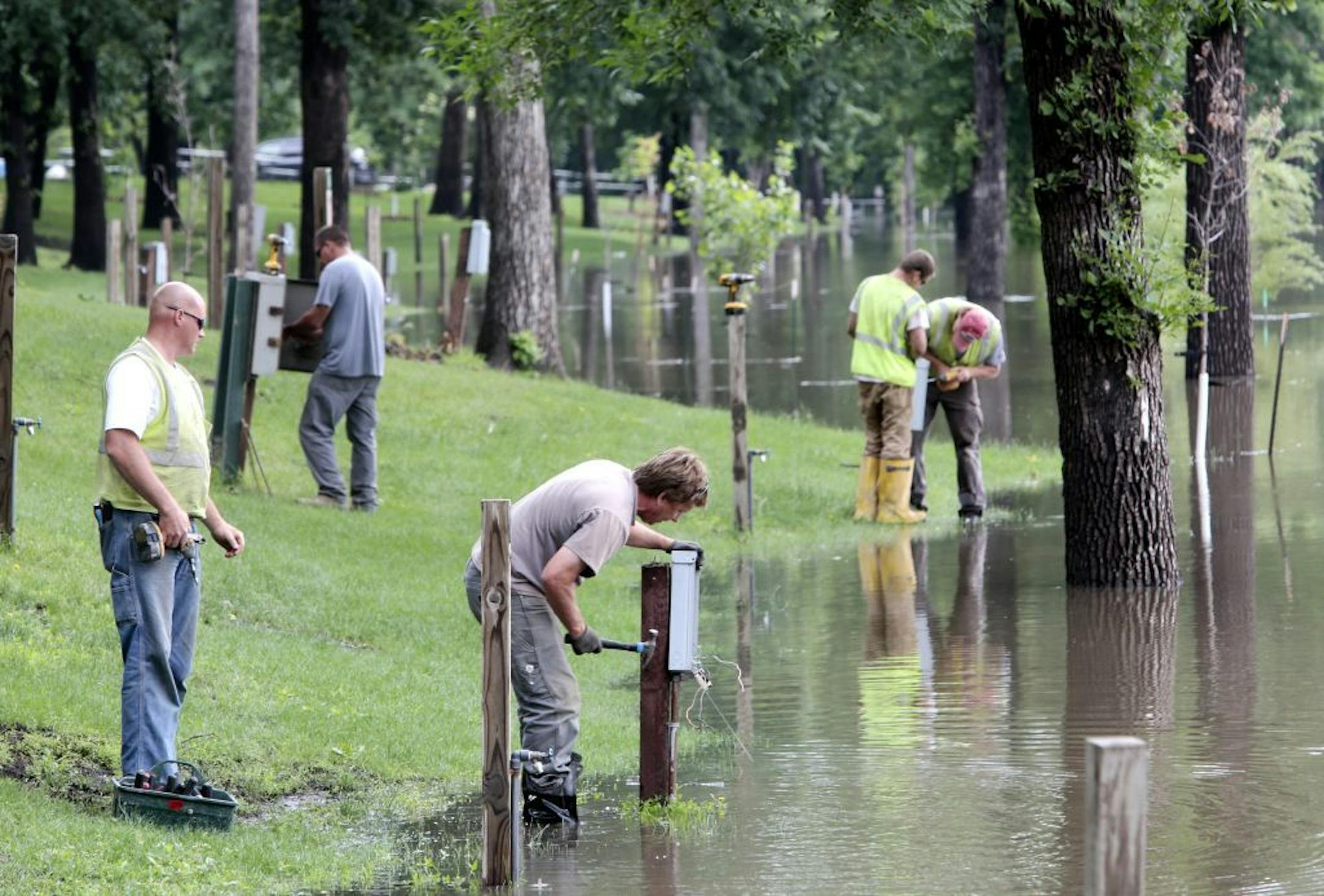 Electric employees Jamie Strom, front, from left, and Jordan Ege work to remove an electrical box from the Lindenwood Campground after the lower camp sites flooded from the Red River on Wednesday, June 26, 2013, following heavy rains in Fargo, N.D.