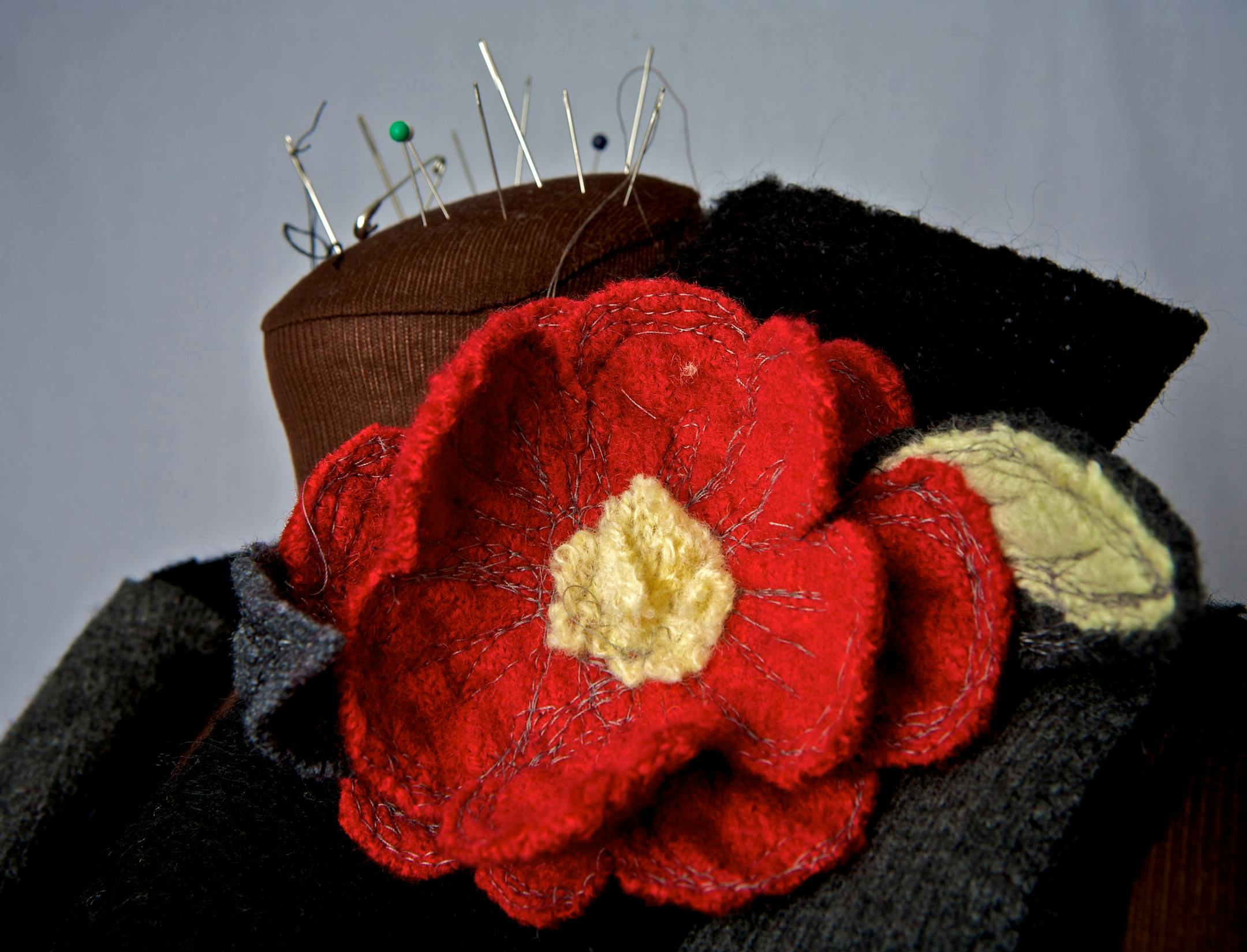 Marsha Theis adds a flower to her finished sweater made from old sweaters that she cuts up and sews to make her own creations.