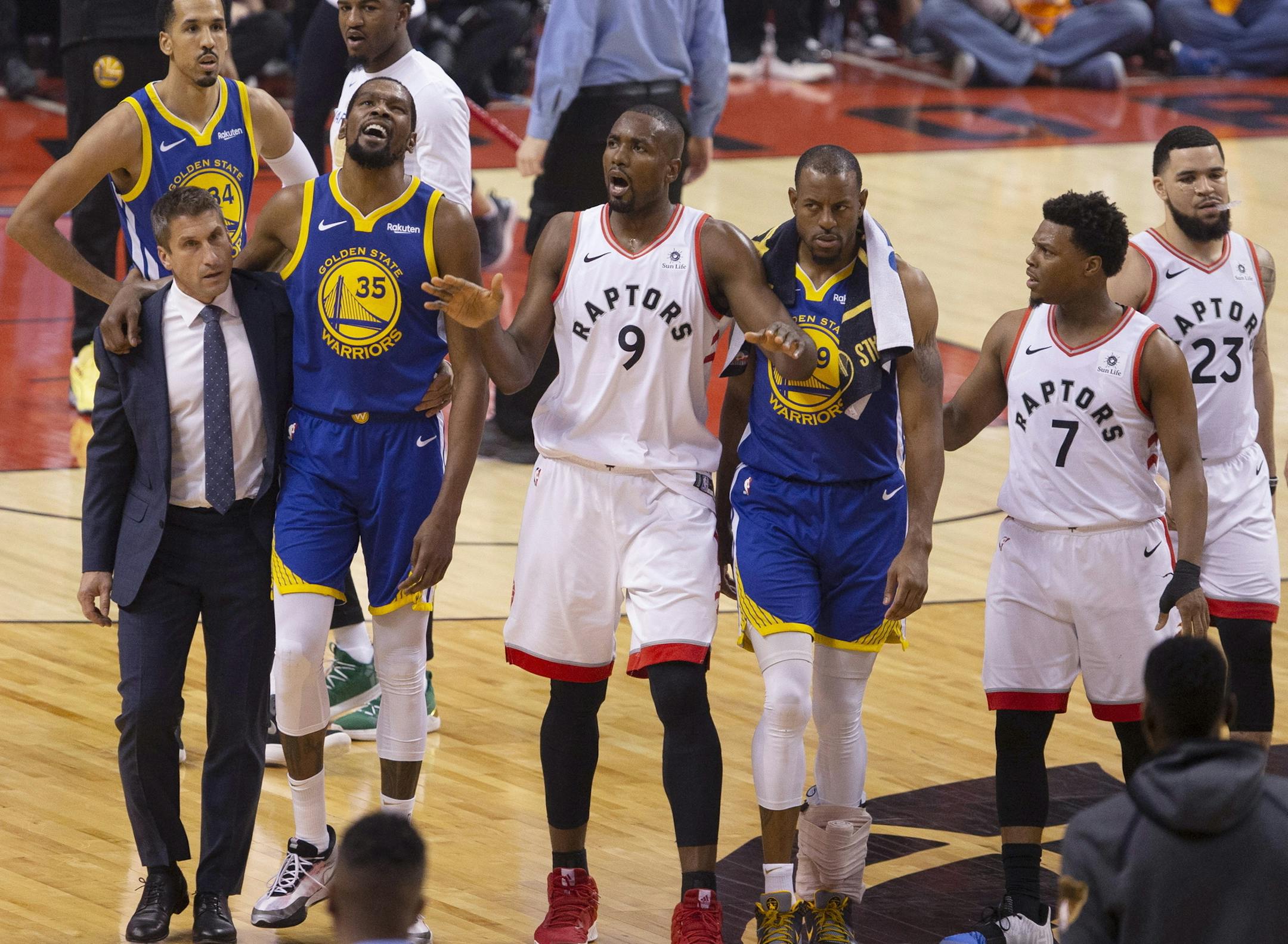 Golden State Warriors' Kevin Durant (35) walks off the court after sustaining an injury as Toronto Raptors' Serge Ibaka (9) addresses the crowd, while Warriors' Andre Iguodala (9) and Raptors' Kyle Lowry (7) look on during first half basketball action in Game 5 of the NBA Finals in Toronto, Monday, June 10, 2019. (Chris Young/The Canadian Press via AP)