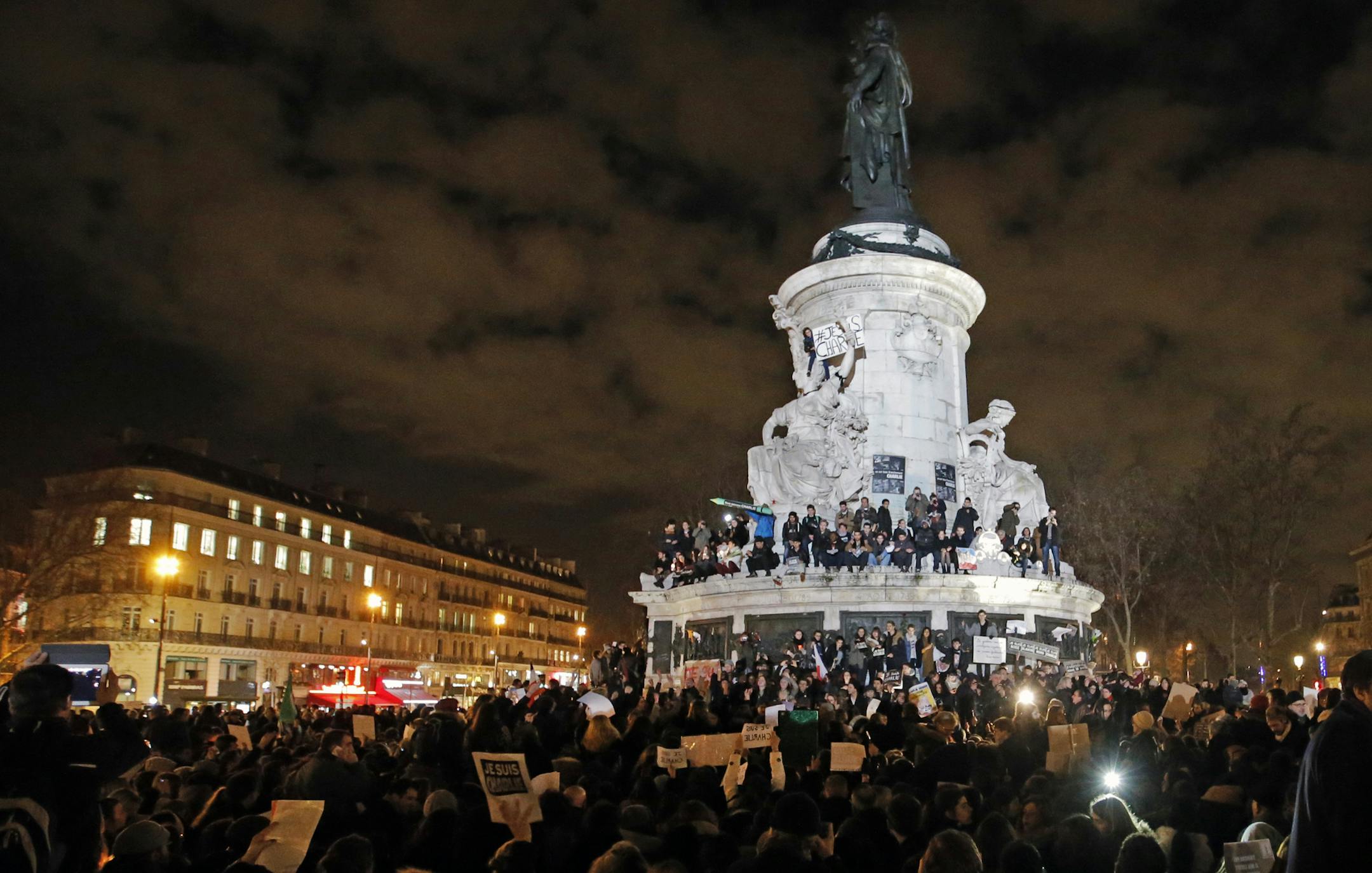 People gather around and ontop of the Republique Plaza statue during the solidarity demonstration in Paris, Thursday, Jan. 8, 2015. Scattered gunfire and explosions shook France on Thursday as its frightened yet defiant citizens held a day of mourning for 12 people slain at a Paris newspaper. French police hunted two heavily armed brothers suspected in the massacre, fearing they might strike again. (AP Photo/Francois Mori)