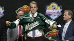 Joel Eriksson Ek, of Sweden, puts on a Minnesota Wild sweater after being chosen 20th overall during the first round of the NHL hockey draft, Friday, 