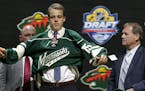Joel Eriksson Ek, of Sweden, puts on a Minnesota Wild sweater after being chosen 20th overall during the first round of the NHL hockey draft, Friday, 