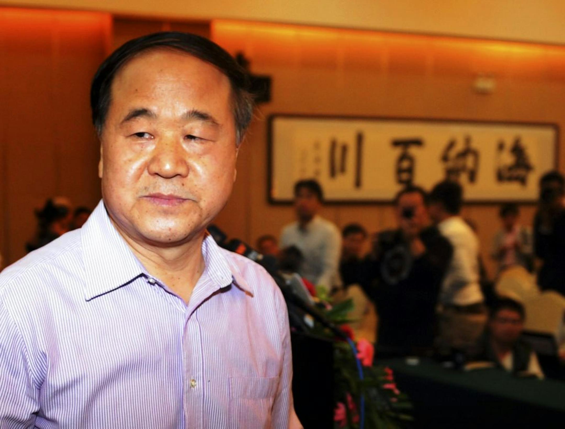 Chinese writer Mo Yan attends a press conference in Gaomi, his hometown, in east China's Shandong province Friday Oct. 12, 2012. Nobel Prize for literature winner Mo Yan has expressed hope that China's imprisoned Nobel Peace Prize winner Liu Xiaobo will regain his freedom. Chinese calligraphy at right reads "all rivers run into the sea" meant to describe something as all encompassing. (AP Photo) CHINA OUT