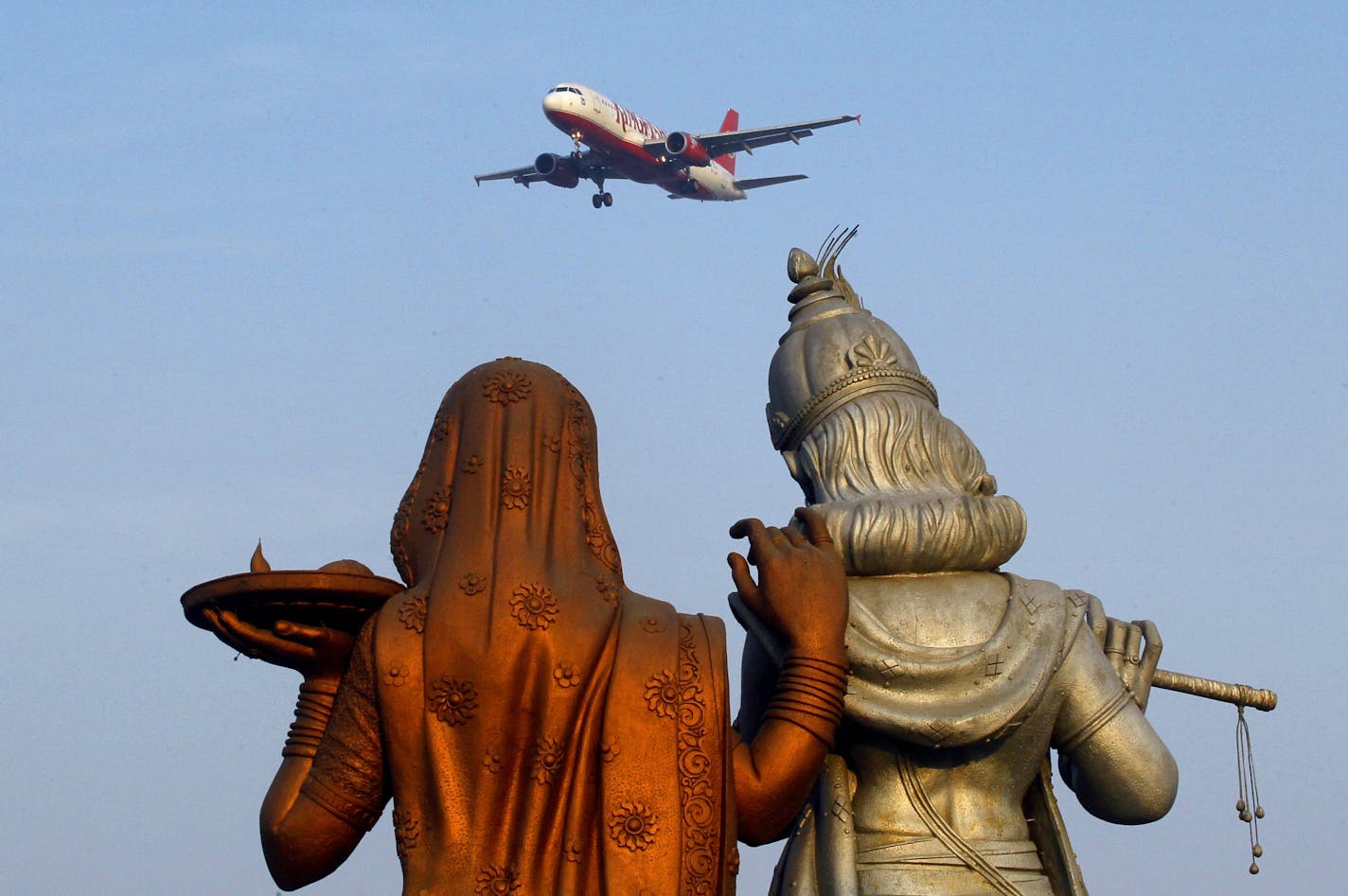 Statue of Hindu Gods Radha, left, and Krishna stand in the foreground as a Kingfisher Airlines flight approaches the Indira Gandhi International airport in New Delhi, India, Friday, Nov. 11, 2011. Kingfisher, which is partly owned by brewery tycoon Vijay Mallya, has canceled more than 120 flights this week as pilots and crew called in sick after their October salaries were delayed.