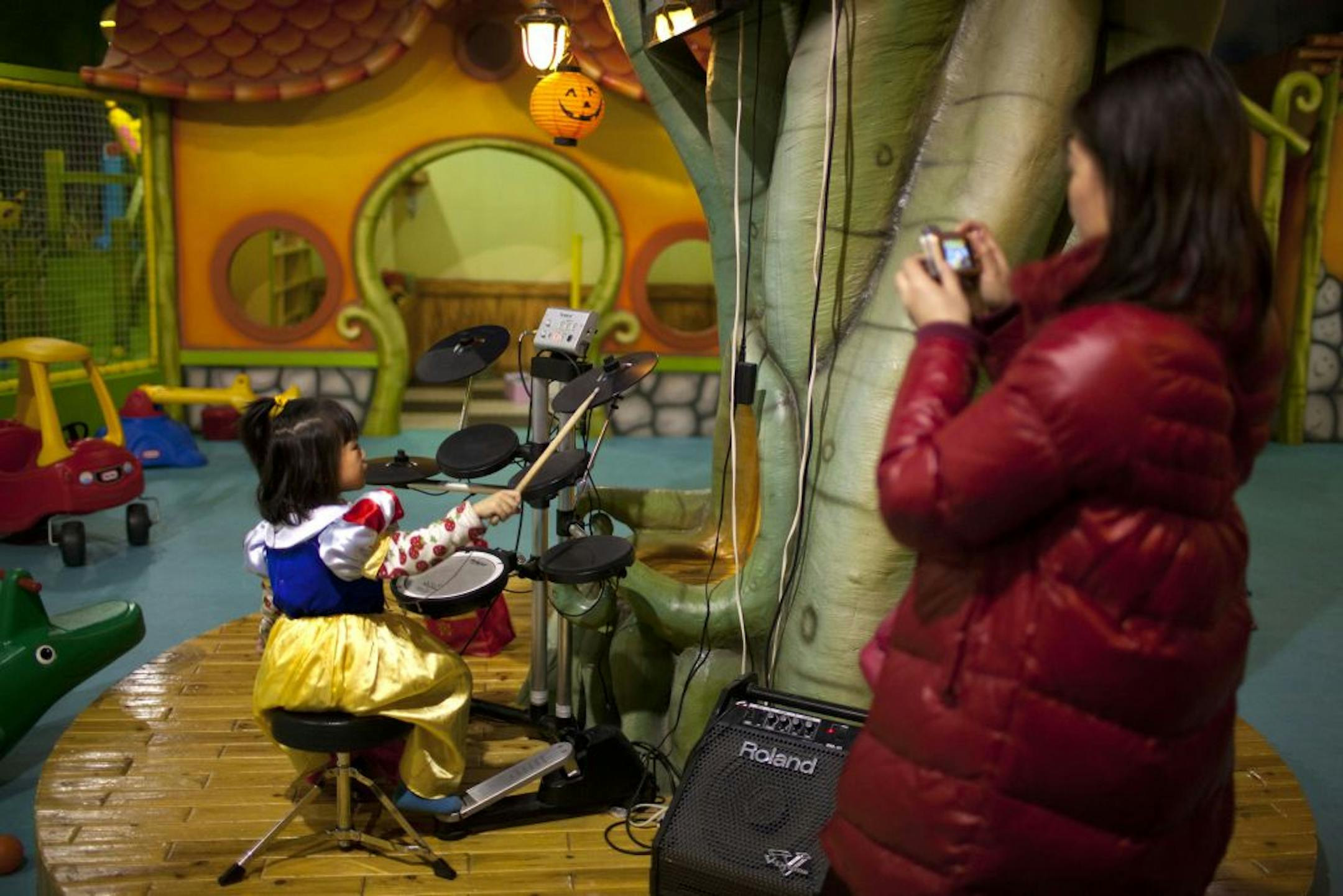 A parent takes photos of her daughter playing the drums at a children's play area in a shopping mall in Beijing Thursday, Jan. 10, 2013. In China, a law generally limits urban families to having just one child. They grow up as the sole focus of doting parents. How does this affect them? What does it mean to Chinese society if generations of kids are raised this way? Authors of a new study say the one-child policy has significant ramifications for Chinese society.