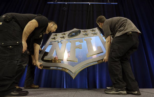 Workers hang an NFL shield on the main stage before a news conference Thursday, Feb. 4, 2016, in San Francisco. (AP Photo/David J. Phillip)