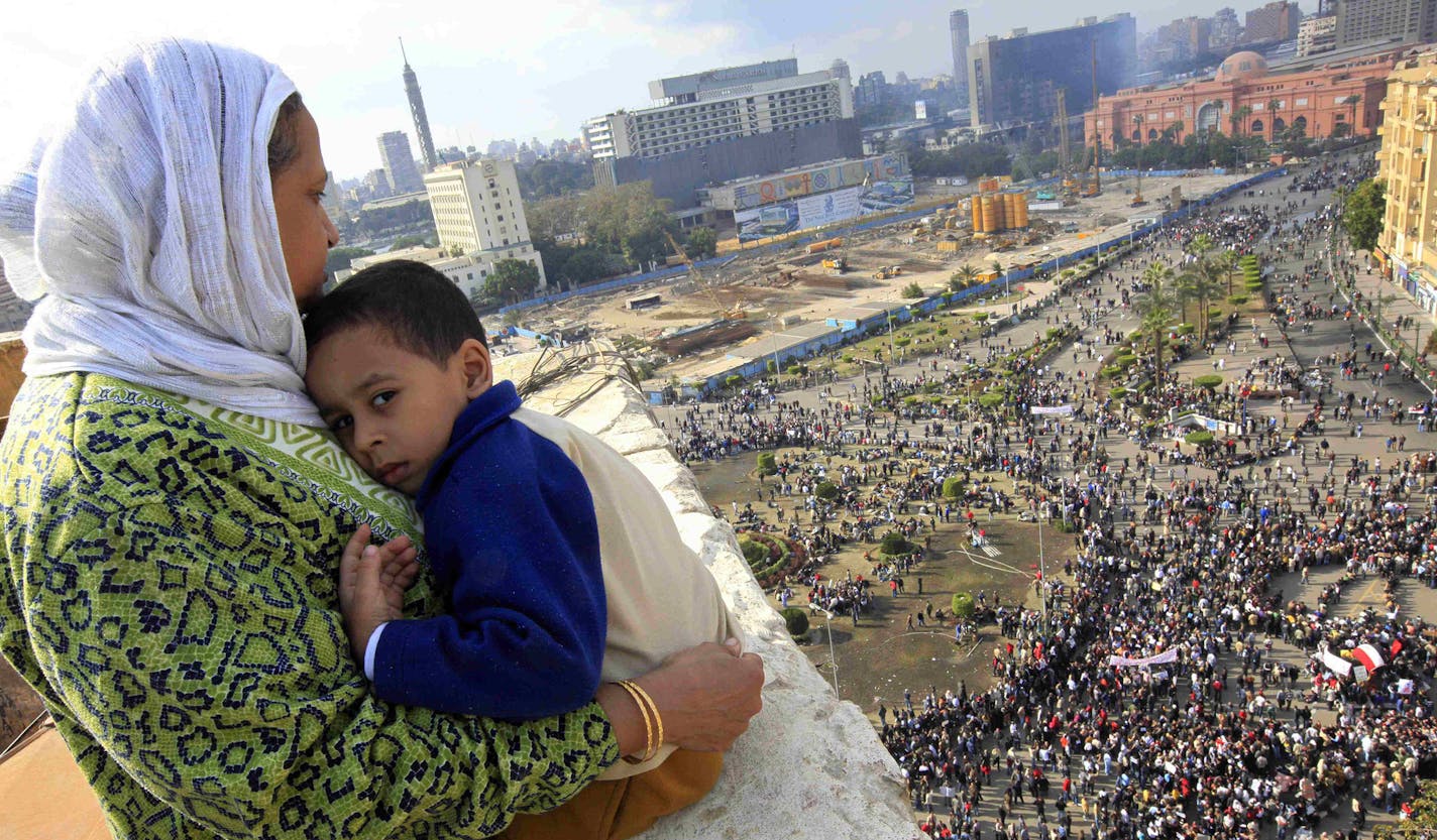 An Egyptian mother hugs her child as she watches some thousands of Egyptian protesters gather at Tahrir square in Cairo, Egypt, Sunday, Jan. 30, 2011, with the ruling National Democratic party building burned at top right behind the red coloured Egypt museum. The army sent hundreds more troops and armored vehicles onto the streets of Cairo and other cities but appeared to be taking little action against mass protests on Sunday. (AP Photo/Amr Nabil) ORG XMIT: MIN2016012210435988