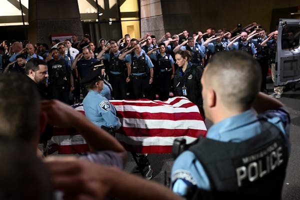 Law enforcement members stand at attention as the casket carrying a Minneapolis police officer is brought to a medical examiner's vehicle outside HCMC