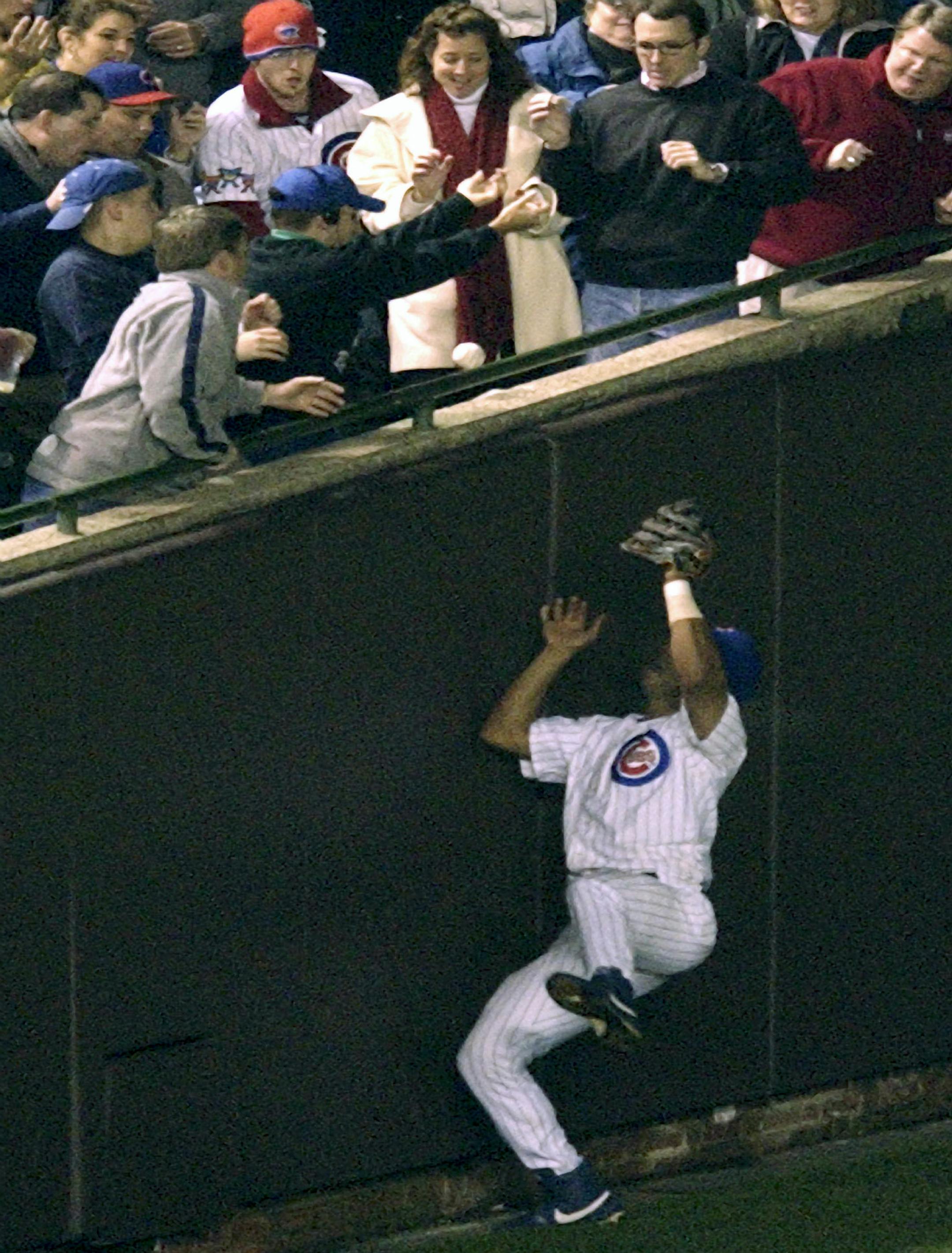 ** FILE ** In this Oct. 14, 2003 file photo, Chicago Cubs left fielder Moises Alou falls back after unsuccessfully reaching into the stands for a foul ball against the Florida Marlins in the eighth inning during Game 6 of the National League championship series at Wrigley Field in Chicago. The ball was caught by spectator, Steve Bartman, shown with his arms out wearing headphones and a Cubs hat. (AP Photo/Amy Sancetta, File) ORG XMIT: NY167