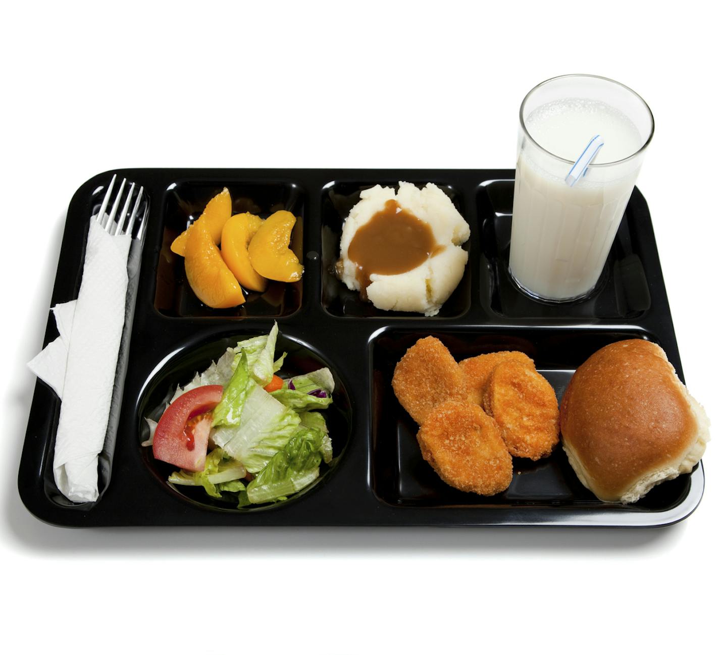 A black school lunch tray including tossed salad, chicken nuggets, roll, peaches, mashed potatoes and gravy with milk on a white background