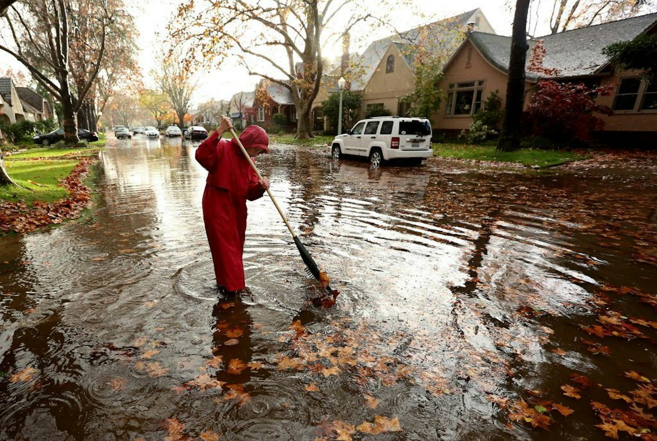 Marilyn Van Schenk stands in knee-deep water as she clears a clogged storm drain that had caused her street to flood in Sacramento, Calif., Wednesday, Dec. 3, 2014.