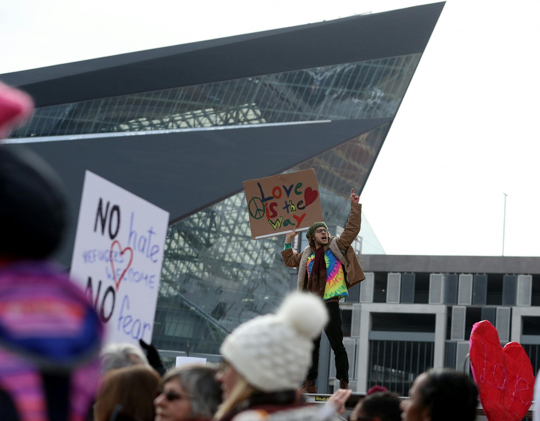 As the march paused for speakers a man hopped up for a higher perspective while displaying his sign with the US Bank Stadium to his rear.
