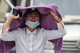A woman used a sweater to shield from the sun as she walked on a street on a hot day in Beijing, Monday, July 3, 2023. Heavy flooding has displaced th