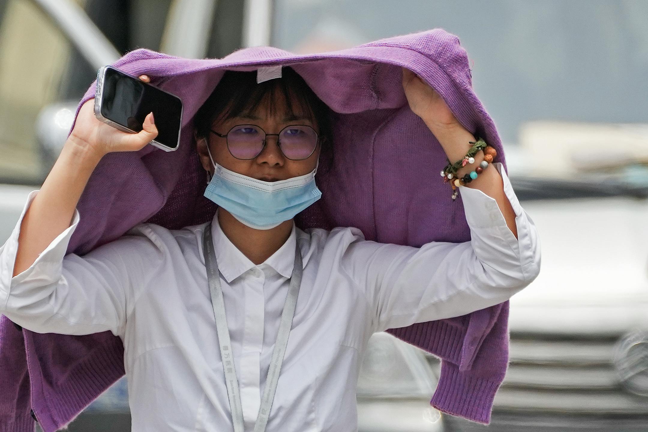 A woman used a sweater to shield from the sun as she walked on a street on a hot day in Beijing, Monday, July 3, 2023. Heavy flooding has displaced thousands of people around China as the capital had a brief respite from sweltering heat. Beijing reported 9.8 straight days when the temperature exceeded 35 C (95 F), the National Climate Center said Monday. (AP Photo/Andy Wong)