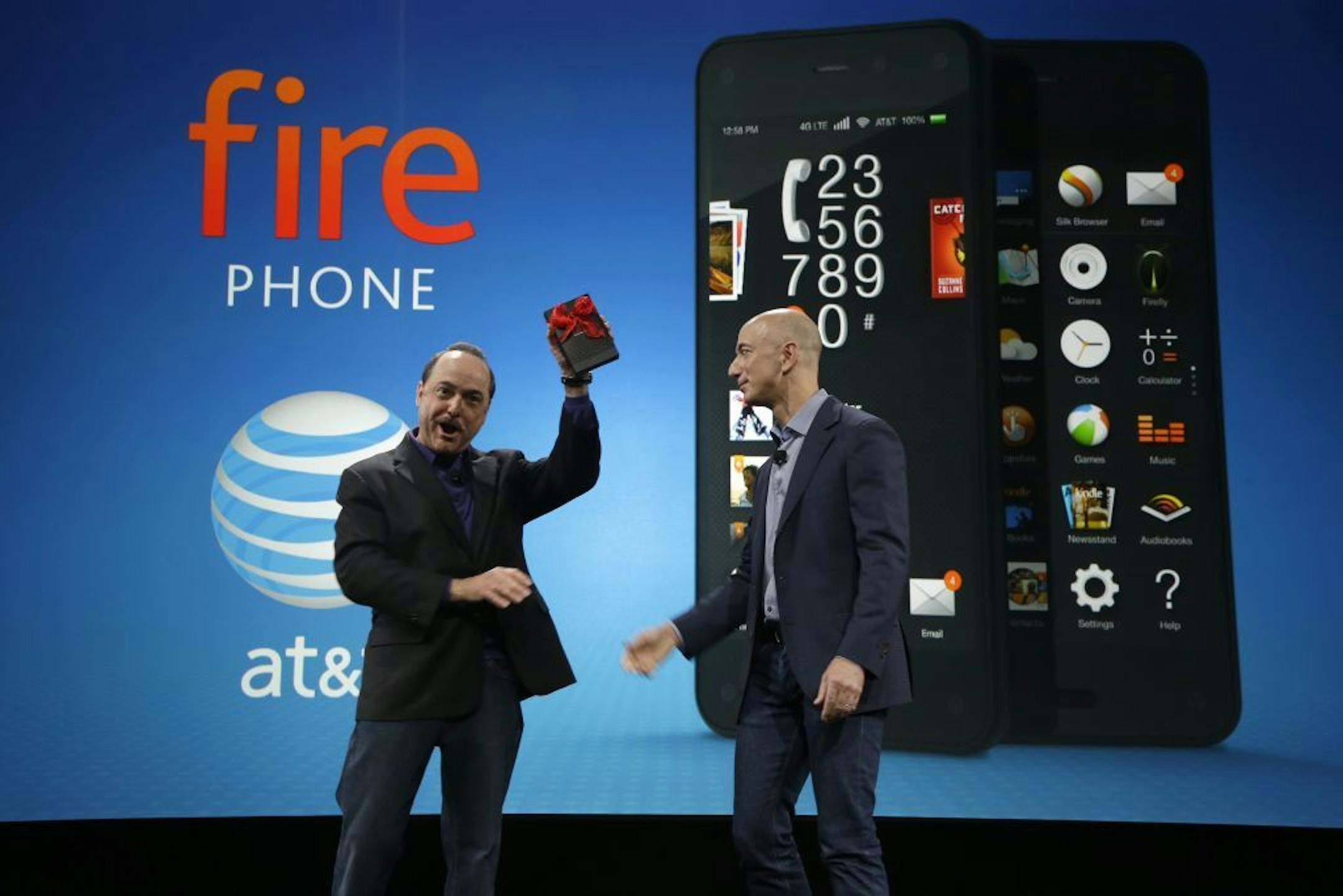 Ralph de la Vega, left, President and CEO of AT&T Mobility, accepts a gift from Amazon CEO Jeff Bezos, right, of what Bezos said is the first Amazon Fire Phone off the assembly line at the launch event for the new smartphone, Wednesday, June 18, 2014, in Seattle. AT&T will be the exclusive carrier for the new phone.