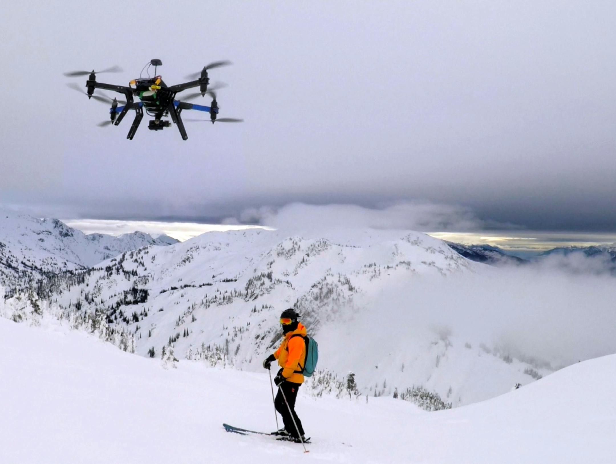 This Dec. 2014 photo shows a drone hovering by a skier as he makes his way down mountainside at resort at Revelstoke, B.C., Canada. Some US ski resorts are exploring the possibility of "drone zones" where professionally operated drones can produce customized video that show off individuals skiers in action. (Jason Soll/Cape Productions via AP)