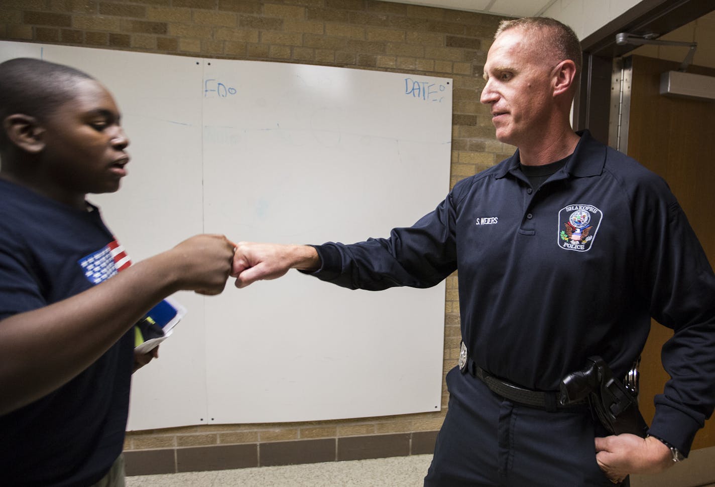 Shakopee Police officer Scott Weiers gets a fist bump from 8th grader T.K. Takang during passing period. ] (Leila Navidi/Star Tribune) leila.navidi@startribune.com BACKGROUND INFORMATION: Shakopee Police officer Scott Weiers patrols the hallway during the passing period at Shakopee West Junior High School on Tuesday, October 18, 2016.