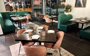 A dining room with a table with four pink chairs in the foreground, and emerald green booths in the background