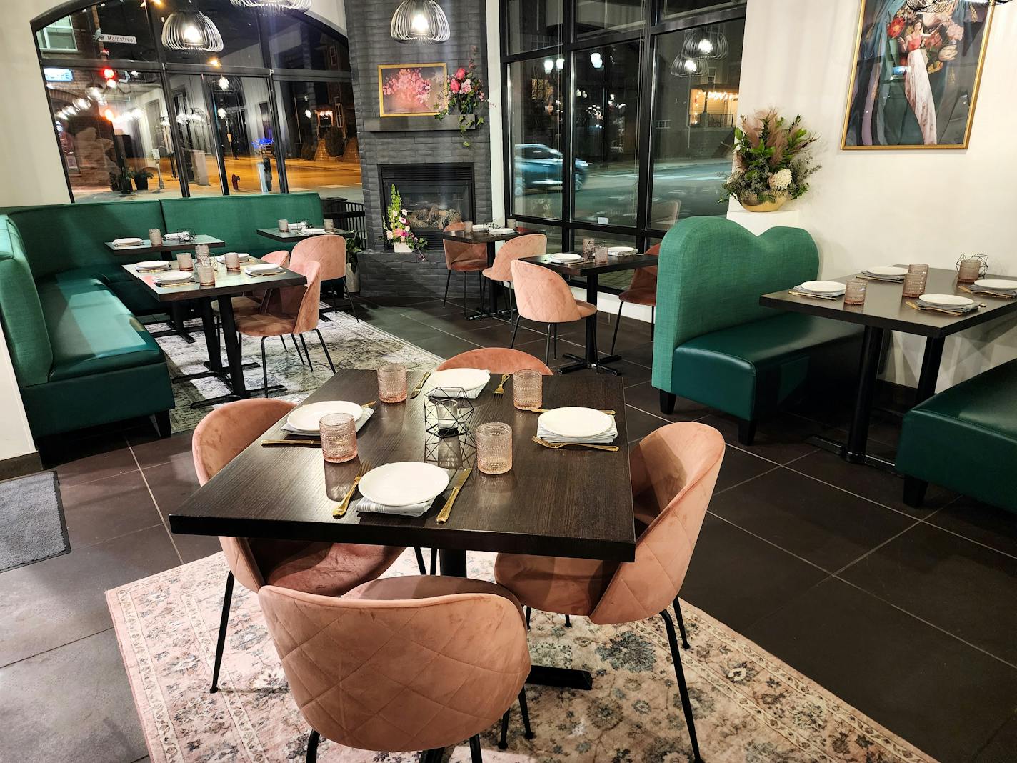 A dining room with a table with four pink chairs in the foreground, and emerald green booths in the background