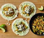 Three tacos topped with avocado crema and a mixture of corn and zucchini.