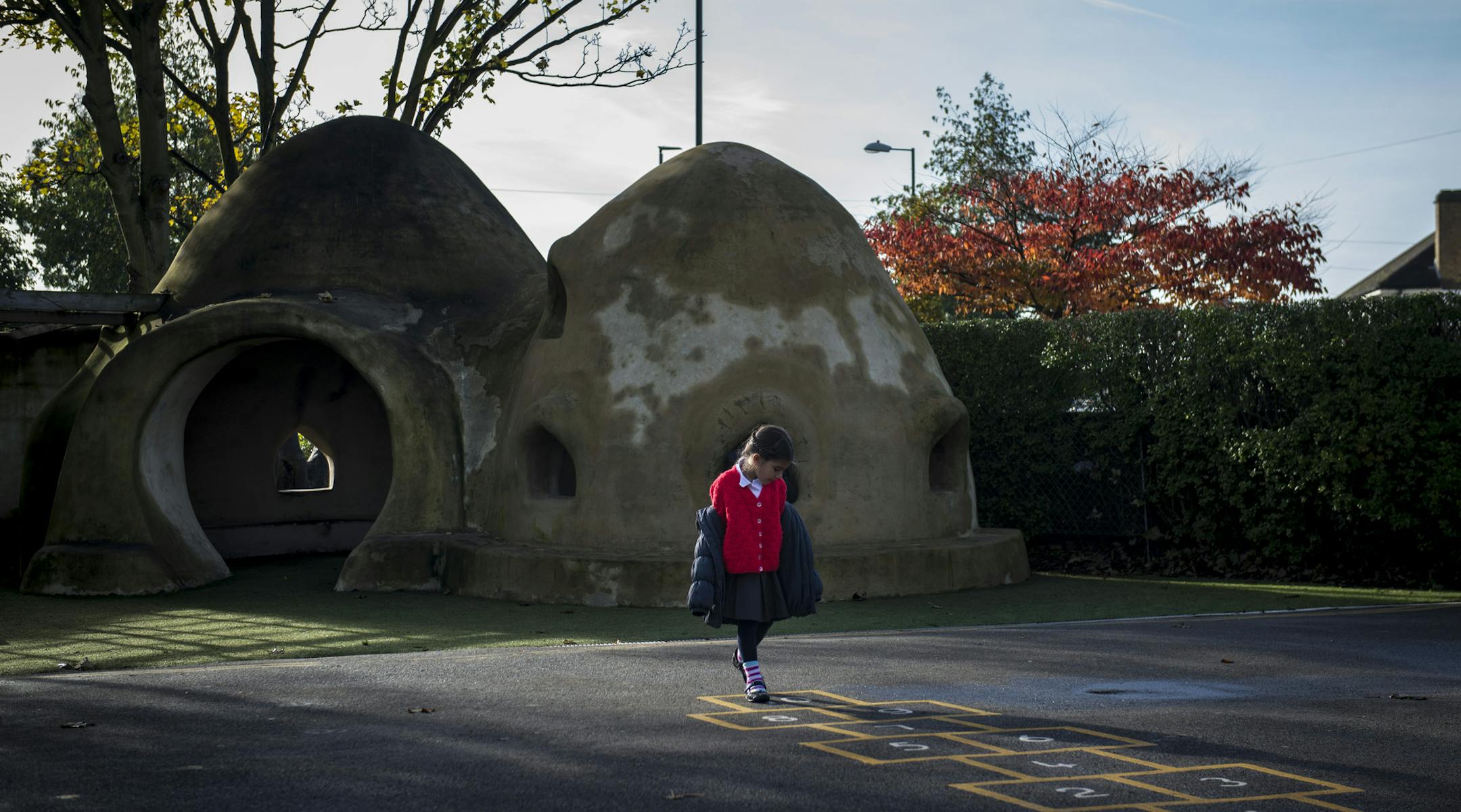 A student next to a "super adobe" dome on the playground at Hounslow Health Infant School, where planes landing at Heathrow Airport can pass every 60 seconds during busy times, in London, Nov. 13, 2013. Heathrow Airport will build similar domes, designed for earthquake zones in Asia and Africa, to protect children in 21 schools from the noise of the third-busiest airport in the world. (Andrew Testa/The New York Times)