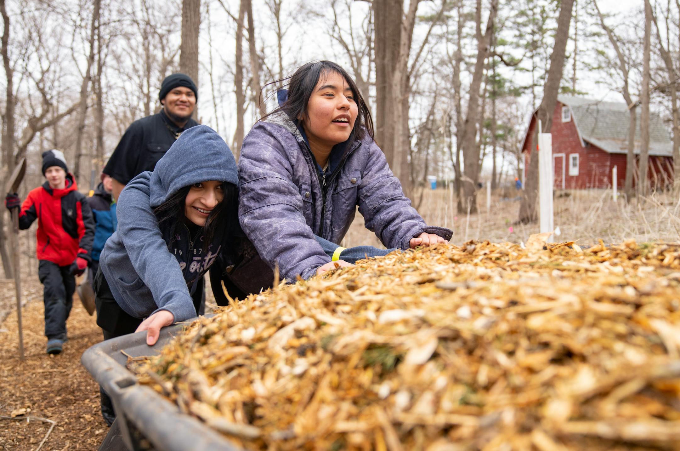 Jackie Gonzalez and Yaretzi Vasquez, left to right, help push a wagon of wood chips as part of a tree planting event Saturday, April 22, 2023, on a Nature Hiking Trail leading to the Minnesota River in Bloomington.