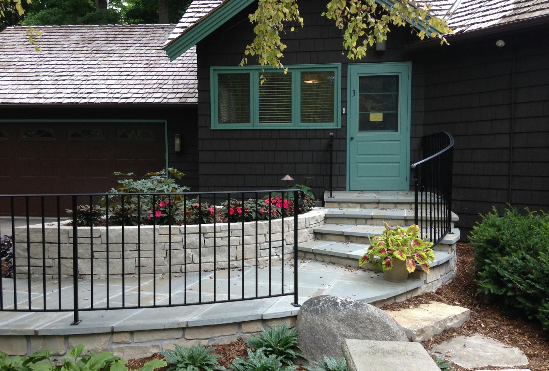 A bluestone sidewalk and steps, next to a curved limestone planter, create a smooth walkway from the driveway to a front entry.