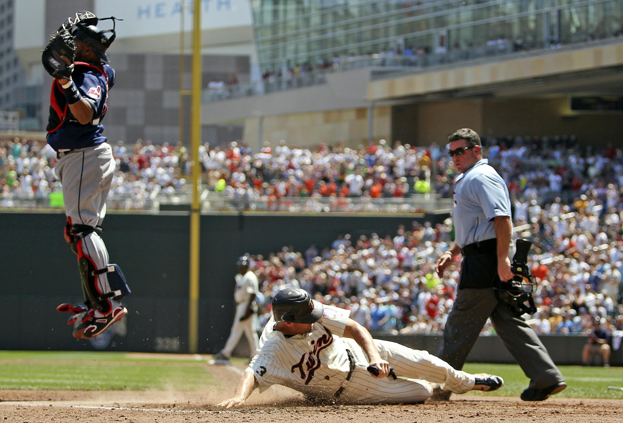 The Minnesota Twins Michael Cuddyer slides safely into home, past Cleveland catcher Carlos Santana on a fourth inning double by Jim Thome.