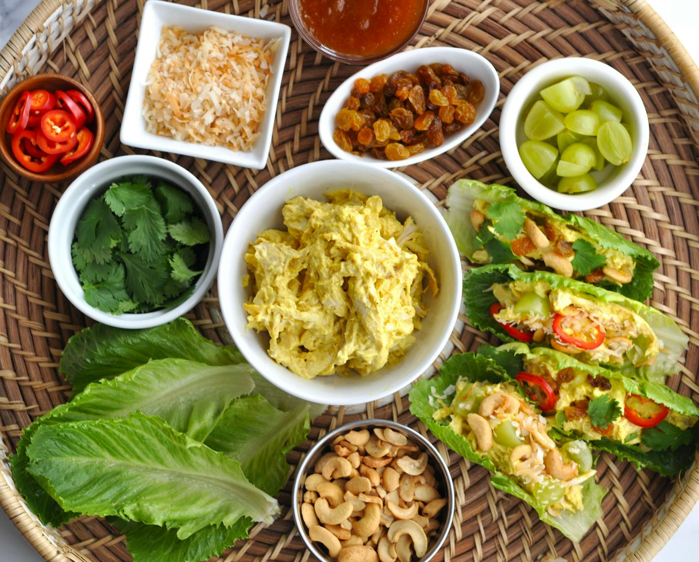 A bowl of chicken curry salad surrounded by bowls of toppings.