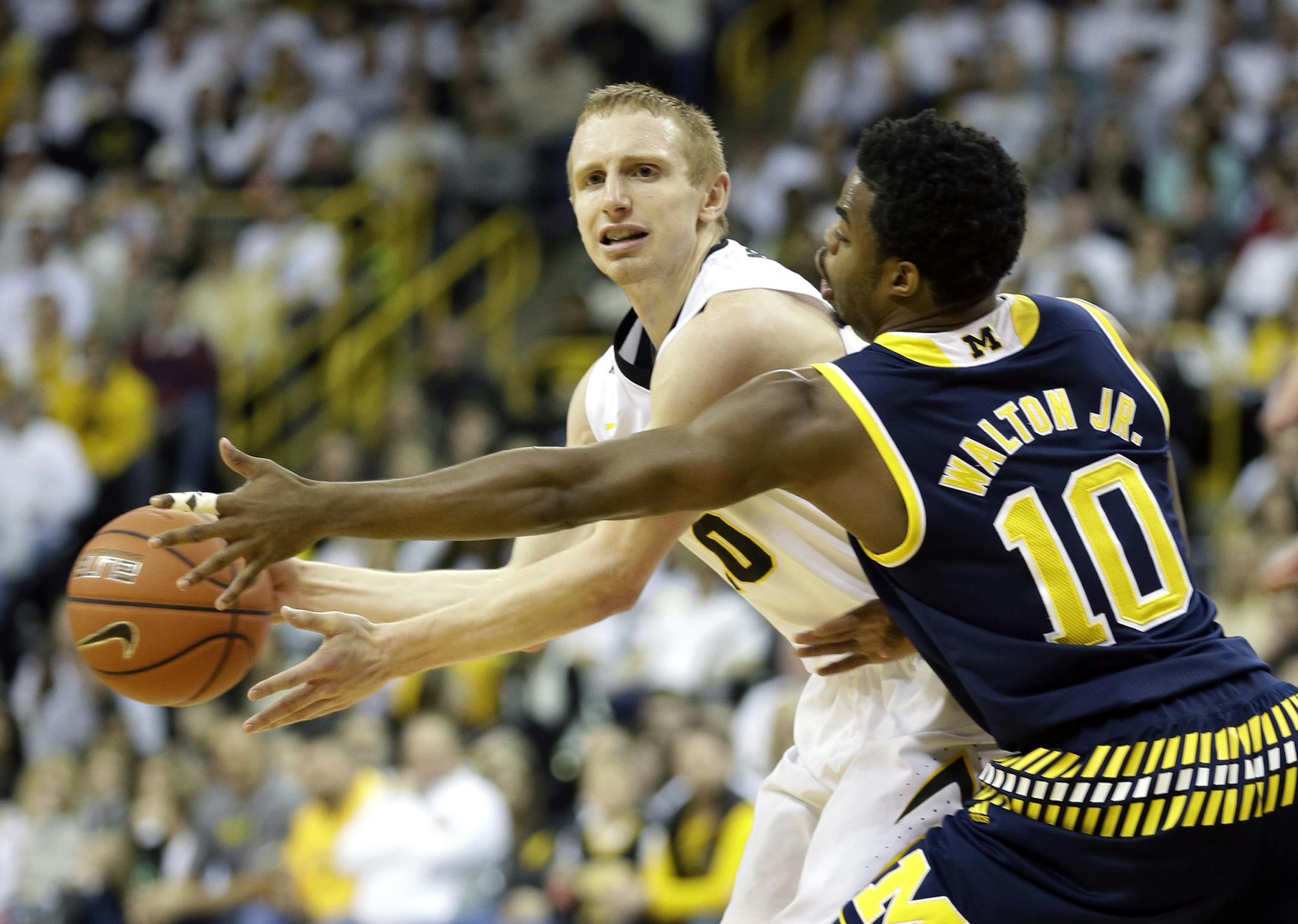 Iowa guard Mike Gesell passes around Michigan guard Derrick Walton Jr., right, during the first half of an NCAA college basketball game, Sunday, Jan. 17, 2016, in Iowa City, Iowa. (AP Photo/Charlie Neibergall)