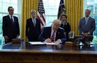 President Donald Trump signs a coronavirus aid package to direct funds to small businesses, hospitals, and testing, in the Oval Office of the White Ho