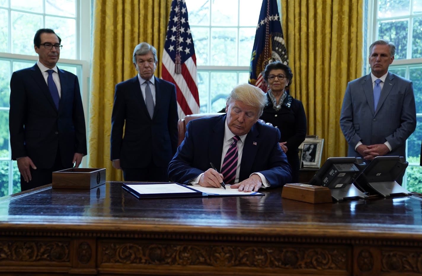 President Donald Trump signs a coronavirus aid package to direct funds to small businesses, hospitals, and testing, in the Oval Office of the White House, Friday, April 24, 2020, in Washington, as from left, Treasury Secretary Steven Mnuchin, Sen. Roy Blunt, R-Mo., Jovita Carranza, administrator of the Small Business Administration, and House Minority Kevin McCarthy of Calif., look on. (AP Photo/Evan Vucci) ORG XMIT: MER6e0b7762947e6969d0bcd1bf0f677