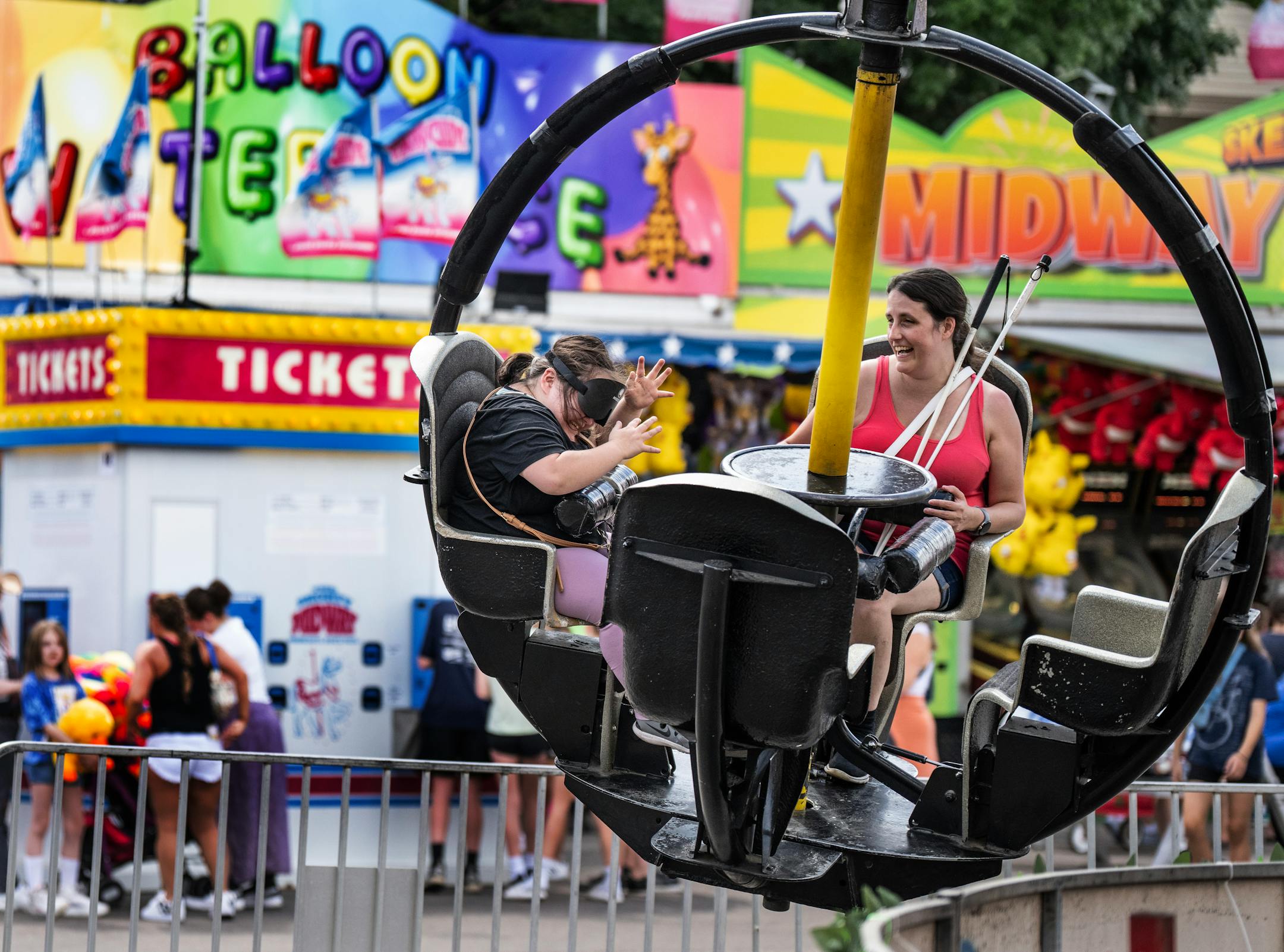 Isabellah Khang 21, left a student at the Blind, Inc. in Minneapolis, shared a ride at the fair with Chelsey Duranleau, Assistant Director BLIND, Inc. Asking thoughtful questions like "Could you tell me where the cheese curd taco stand is from here?" helps the group have a better understanding of how they can get to where they want to go.