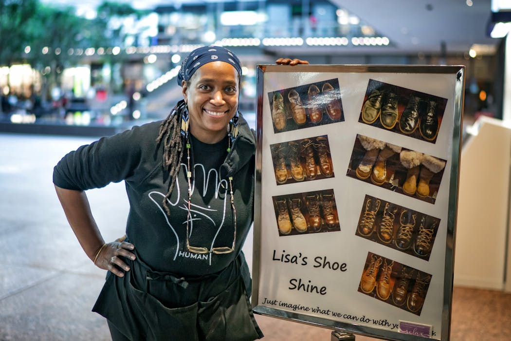 Lisa Cotton stands beside a display of “before and after” pictures of her work outside her storefront at the IDS Center in downtown Minneapolis. Cotton was a calming, caring presence during her 31 years of shining shoes.